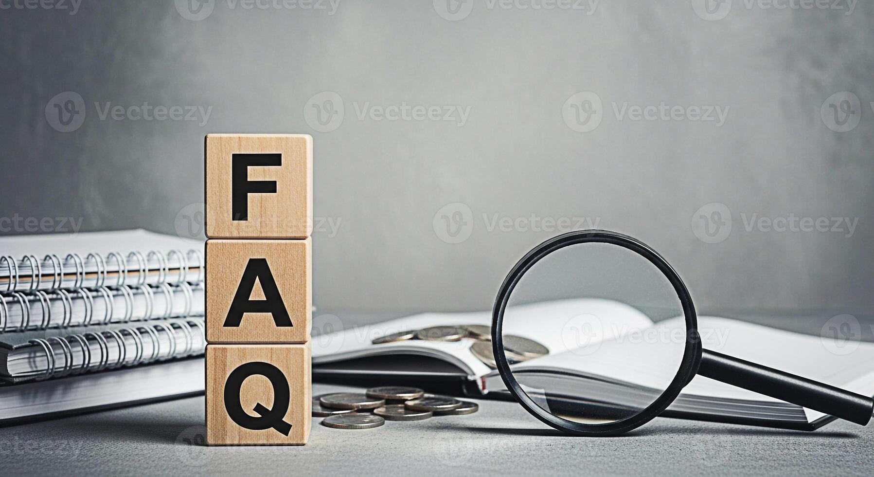 Wooden blocks spelling FAQ on a gray surface with a magnifying glass and coins representing frequently asked questions and financial inquiries in a neutral and informative setting photo