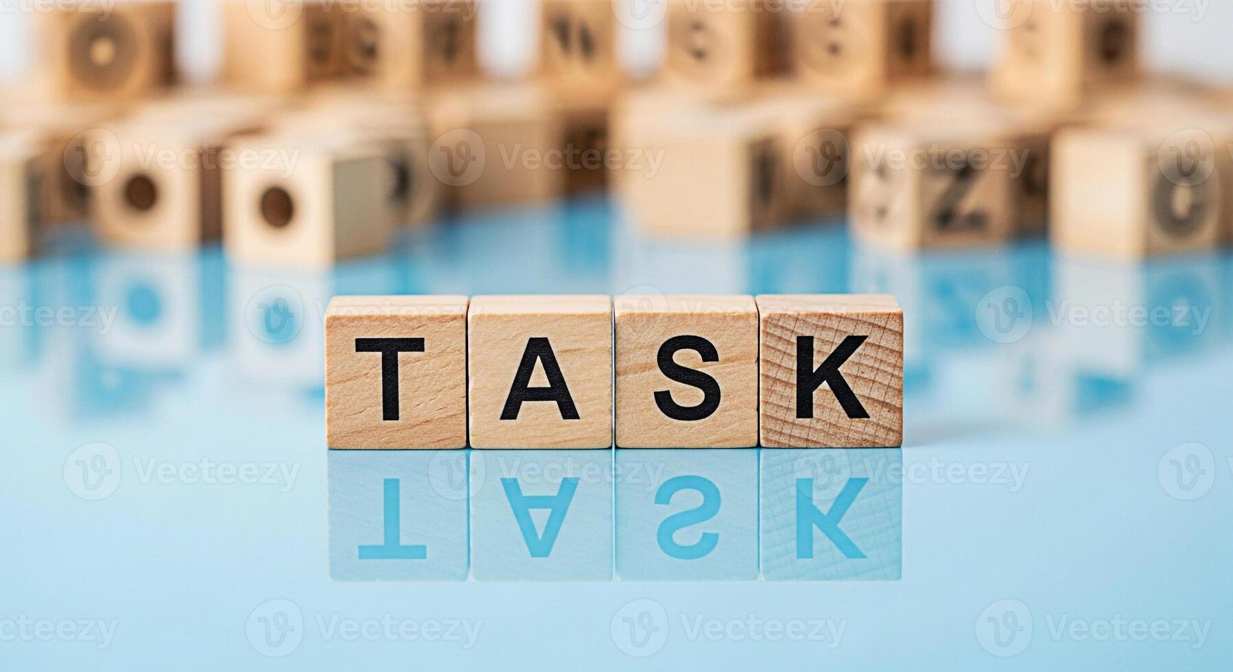 Wooden blocks spelling out TASK on a reflective blue surface surrounded by blurred alphabet blocks representing focus and the importance of completing assignments projects and responsibilities with cl photo