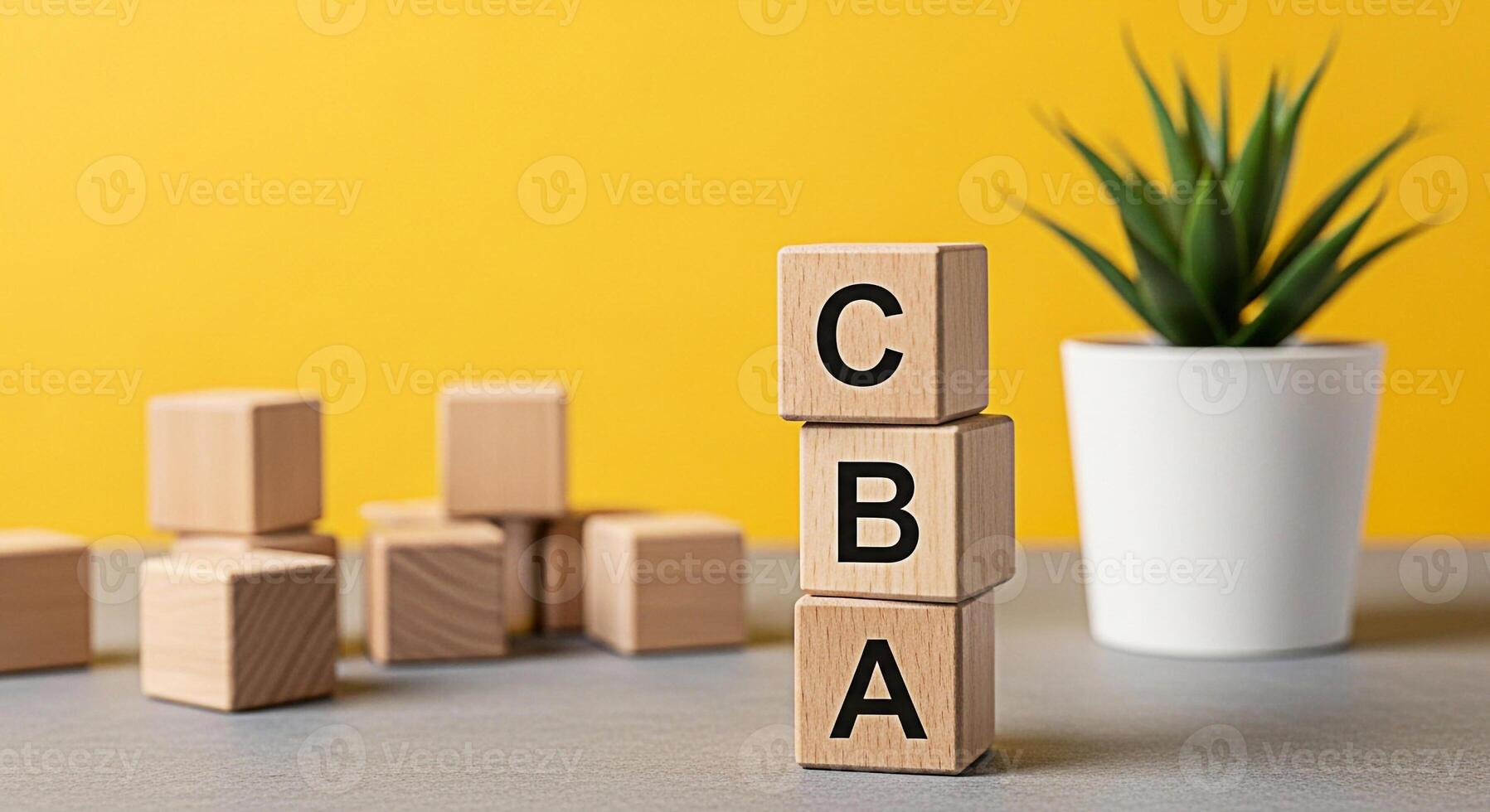 Stack of wooden blocks spelling CBA on a gray surface with a vibrant yellow background and a potted plant representing the concept of basics learning and building blocks of knowledge photo