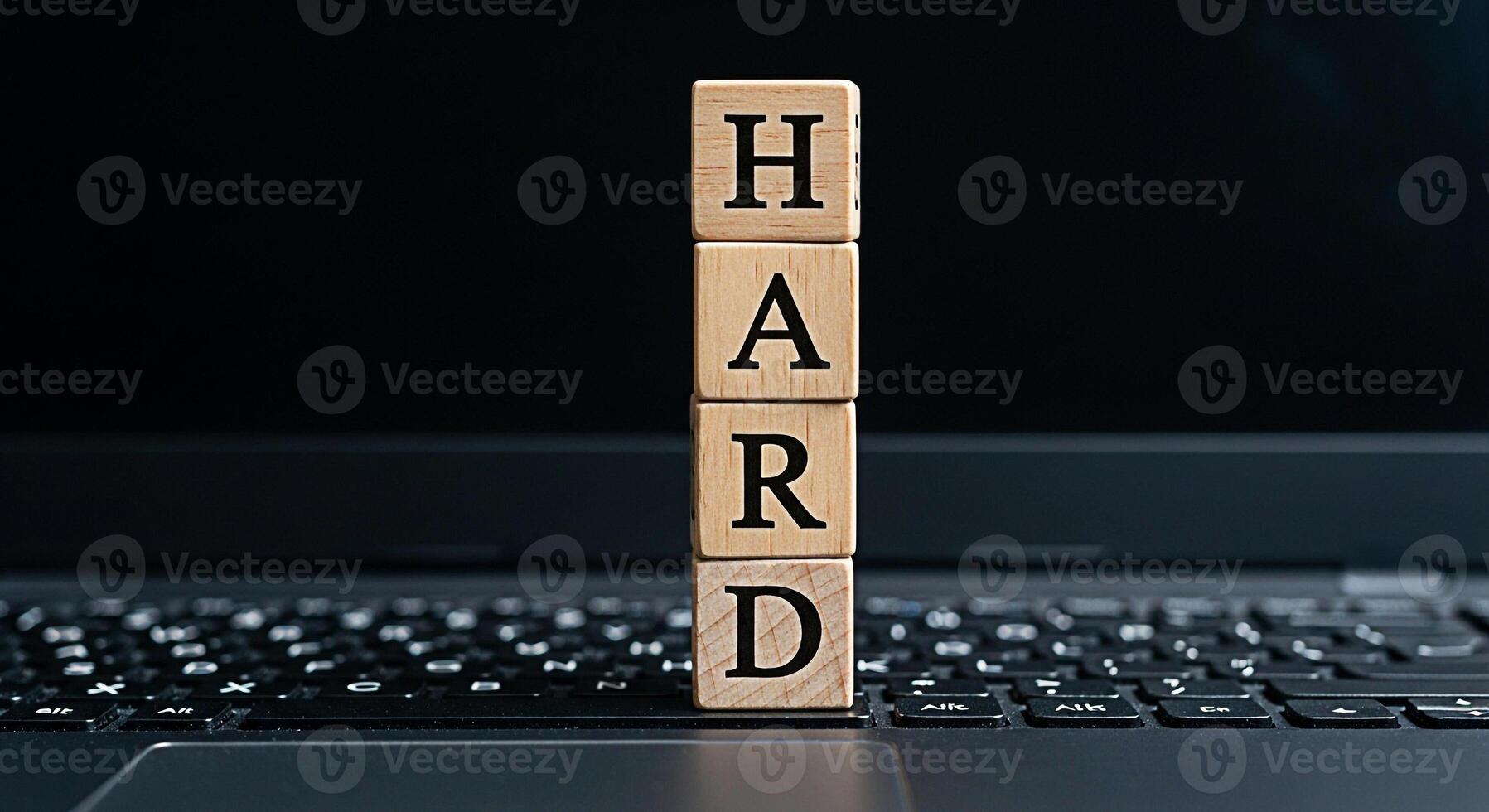 Wooden blocks spelling HARD placed on a laptop keyboard in a dimly lit office symbolizing the concept of challenging work dedication and the effort required to achieve success in the digital age photo