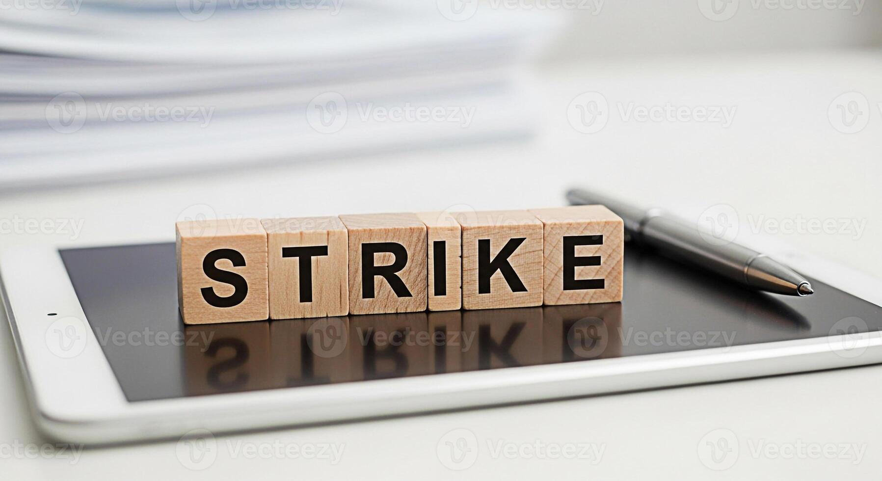 Wooden blocks spelling STRIKE resting on a tablet in a bright modern office environment symbolizing labor disputes union action and the potential for disruption and change in the workplace photo