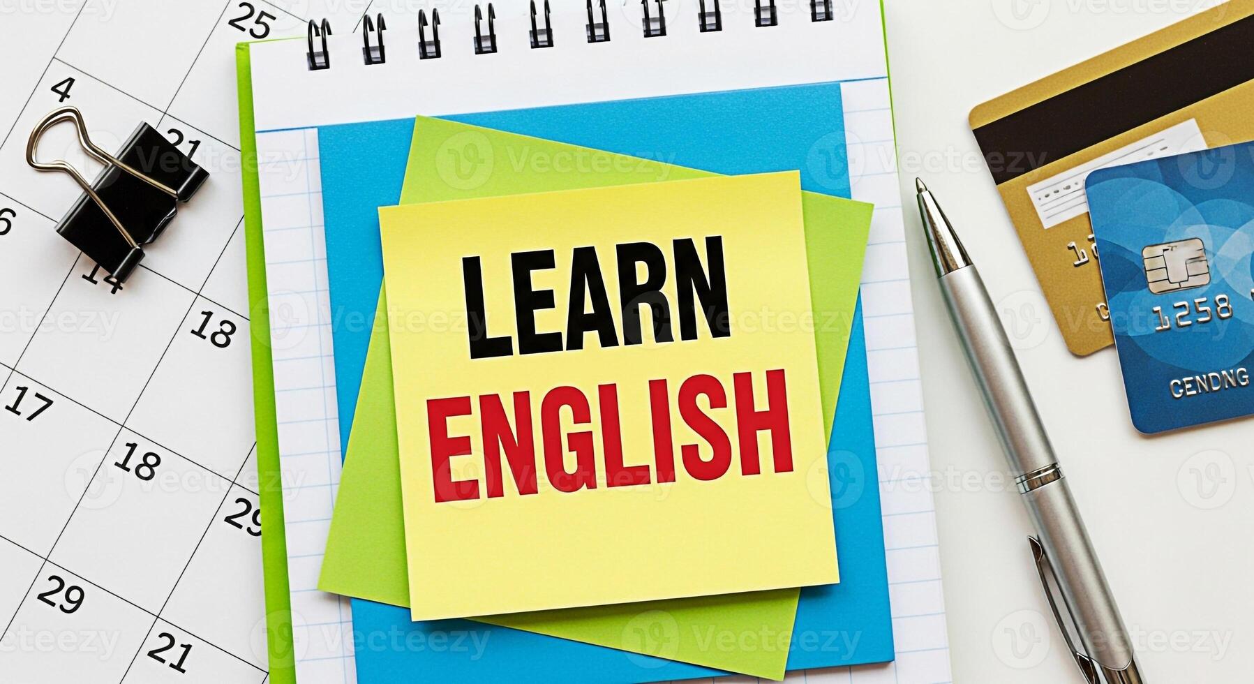 Closeup of a notebook with a sticky note encouraging to learn English placed on a calendar with credit cards and a pen symbolizing education financial planning and time management in a modern workspac photo