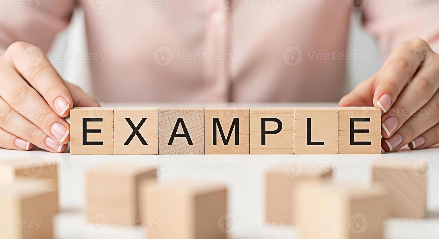 Womans hands arranging wooden blocks spelling EXAMPLE on a white table in a bright clean environment representing clarity demonstration and understanding of concepts and processes photo