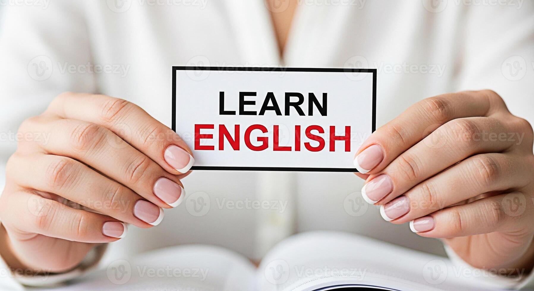 Womans manicured hands holding a card with the text Learn English over an open book symbolizing language acquisition and educational opportunity in a bright optimistic setting photo
