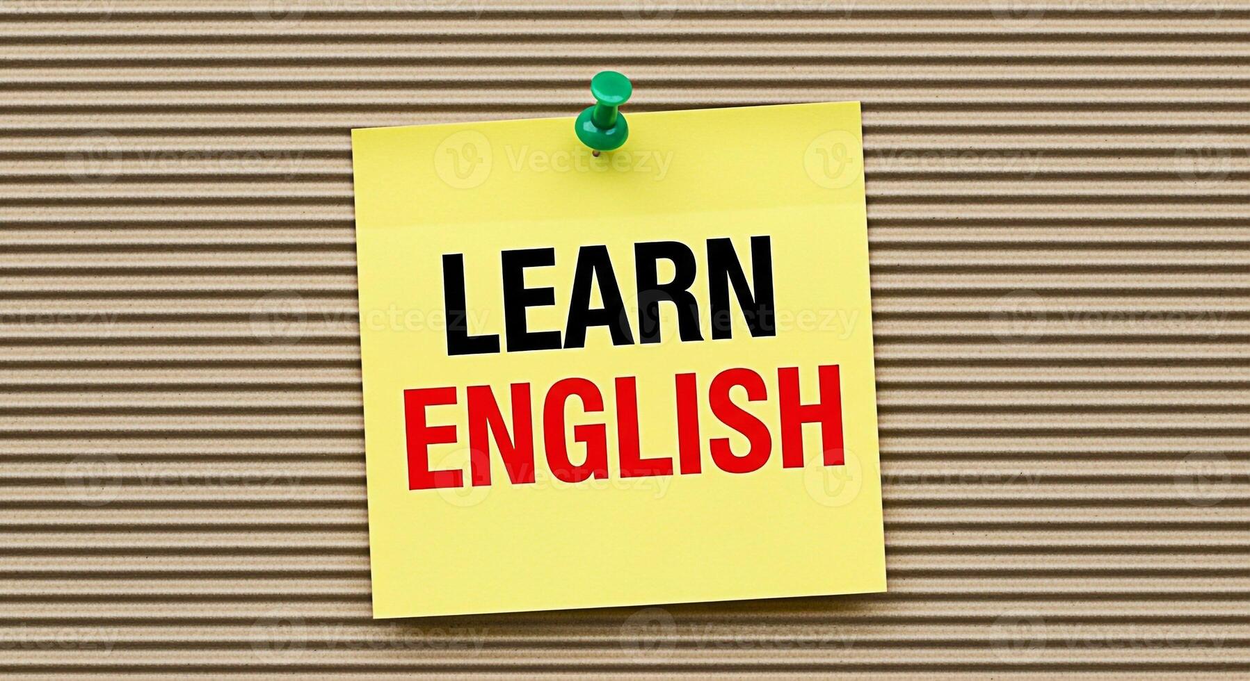 Bright yellow sticky note pinned on a corrugated cardboard background displaying the message Learn English in bold black and red letters symbolizing education language acquisition and a positive learn photo