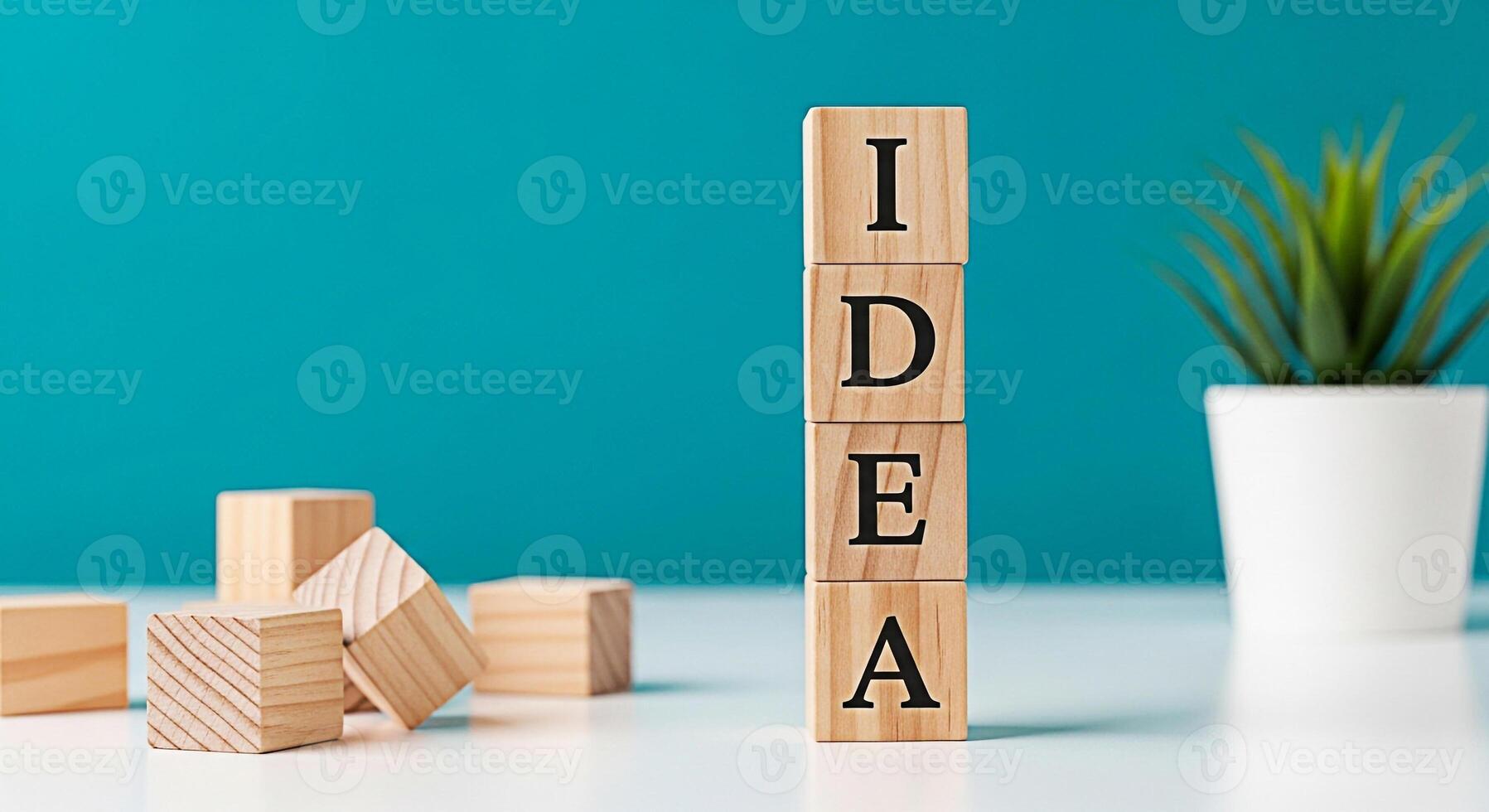 Wooden blocks spelling IDEA stacked on a white table with a green plant against a teal background representing creativity innovation and the generation of new concepts in a bright and inspiring settin photo