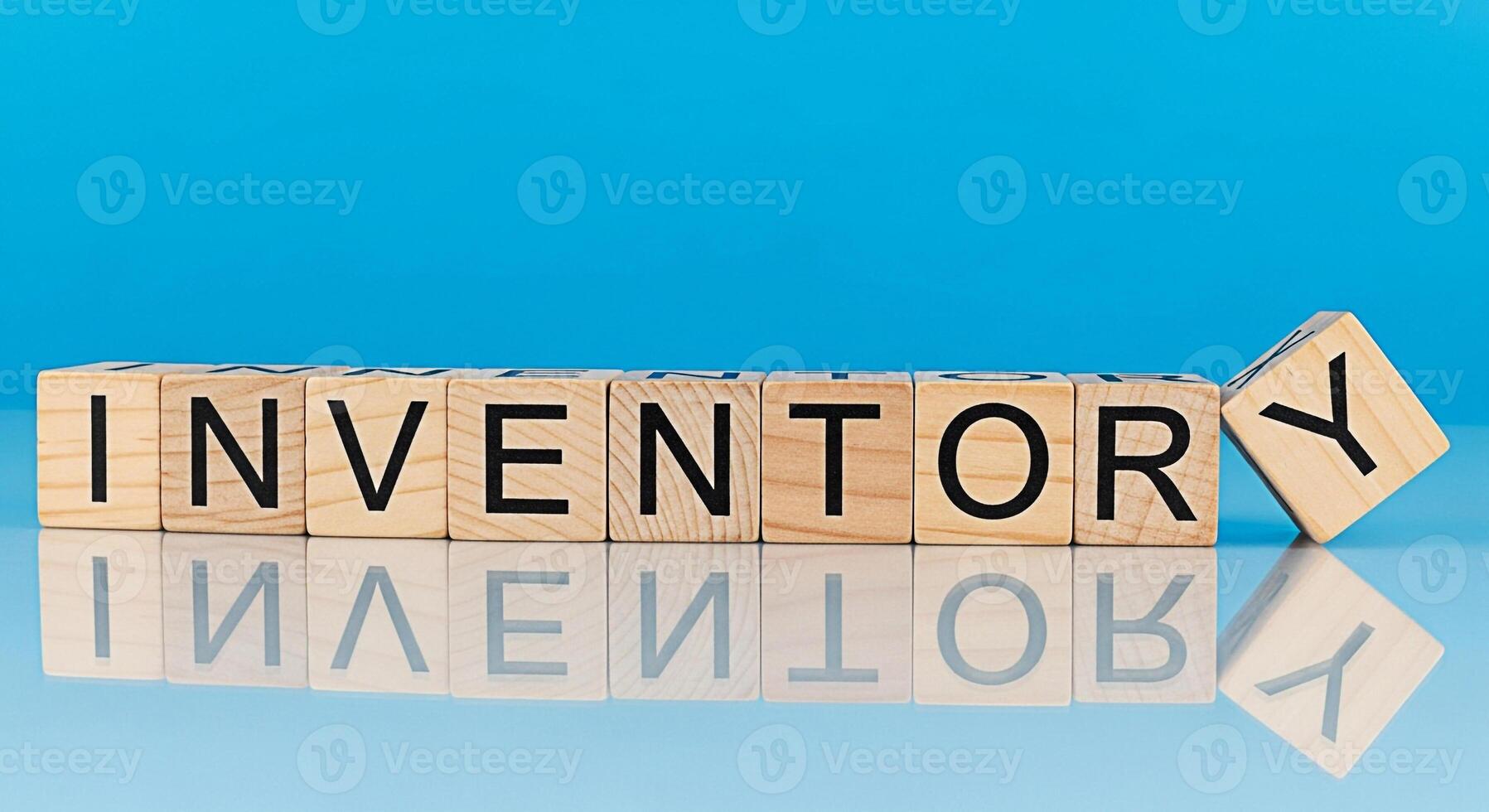 Wooden blocks spelling INVENTORY on a reflective surface against a blue background representing stock management and supply chain efficiency with a focus on organization and control photo