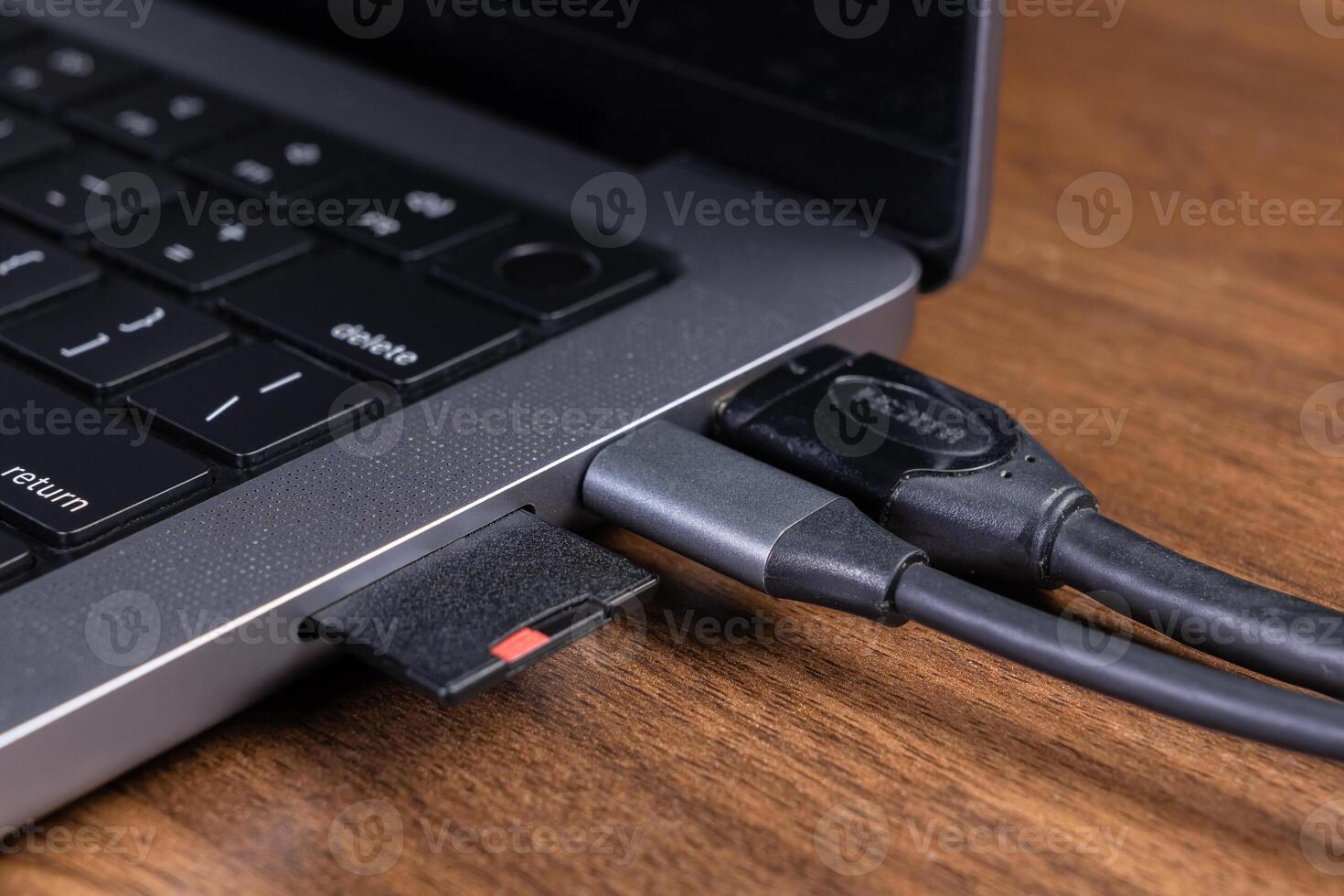 Modern gray laptop on a wooden desk with an inserted SD card, connected USB-C hub, and HDMI cable, for versatile digital data transfer and external display photo