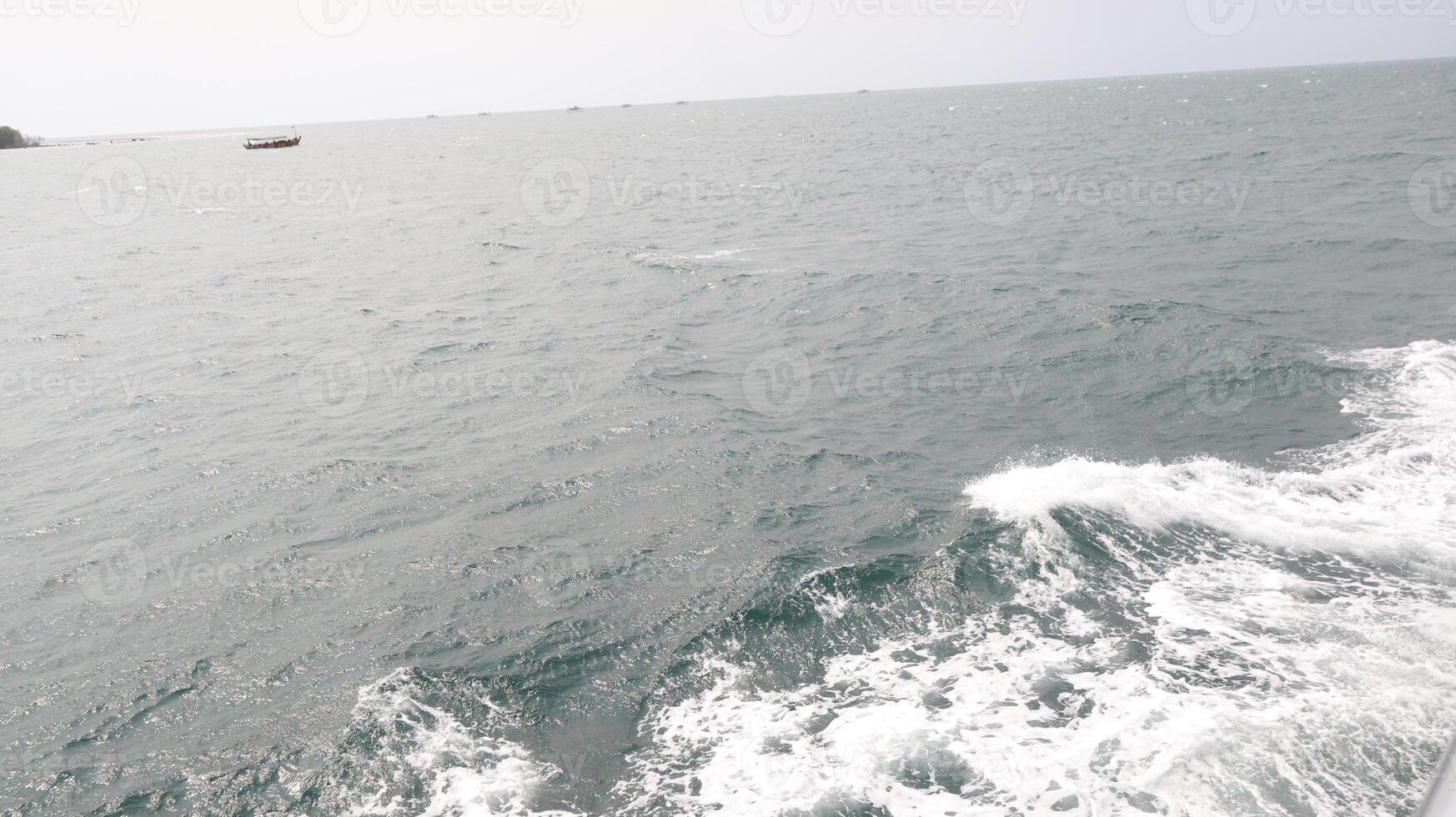 Boat sails on the open ocean during a cloudy day, leaving a trail of white foam and waves, creating a sense of freedom and adventure. photo