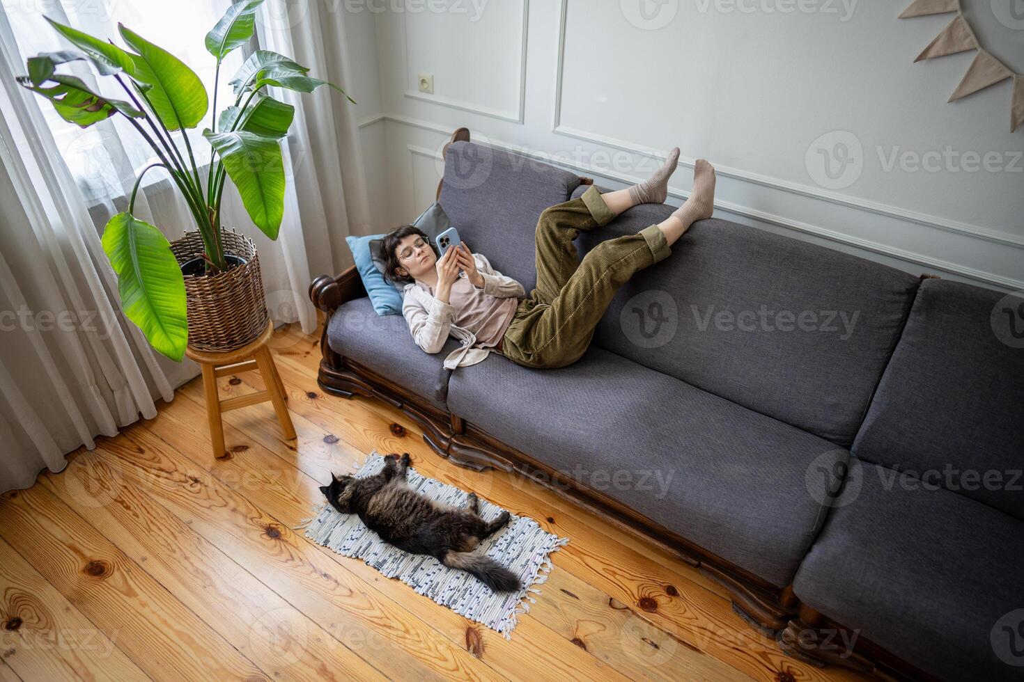 Lazy bored woman lounging on sofa scrolling through smartphone web content as cat rests close by photo
