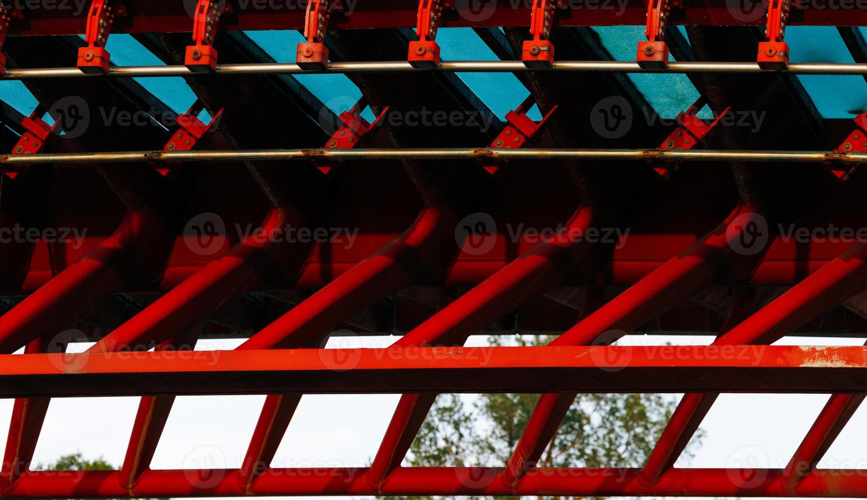 Red and blue roller coaster rail with geometric patterns and trees in background photo