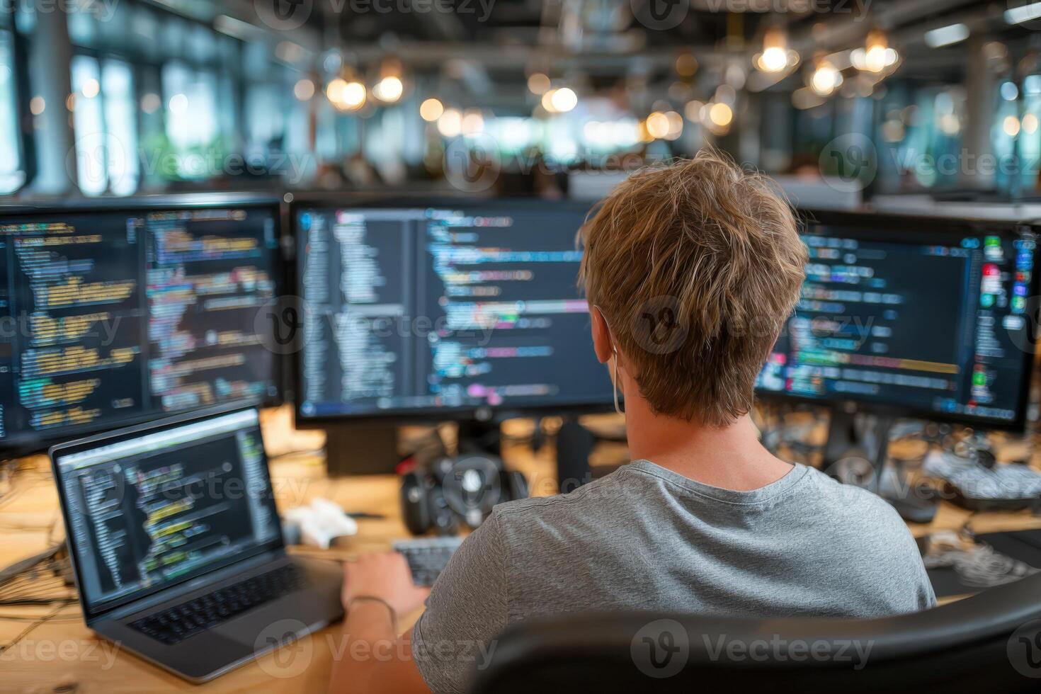 Male software developer working at a modern office desk with multiple monitors displaying code, showcasing a collaborative tech environment and innovative workspace design photo