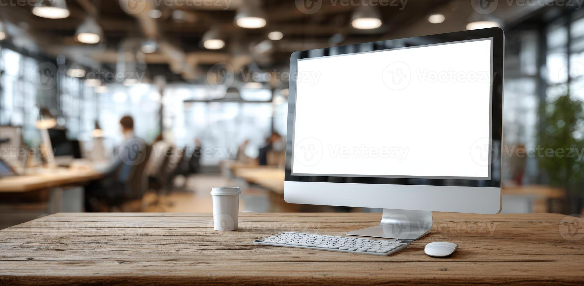 Modern workspace featuring a computer monitor with blank screen, coffee cup, and keyboard on a wooden desk, surrounded by a contemporary office environment with natural light photo