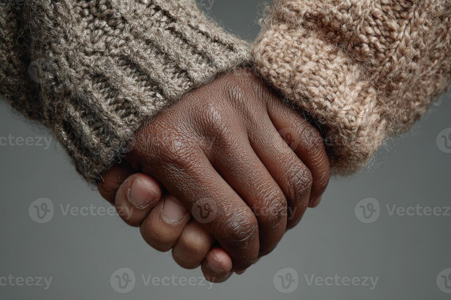 Hands of two individuals, one with dark skin and the other with light skin, clasped together, showcasing unity and connection in a warm, textured setting photo