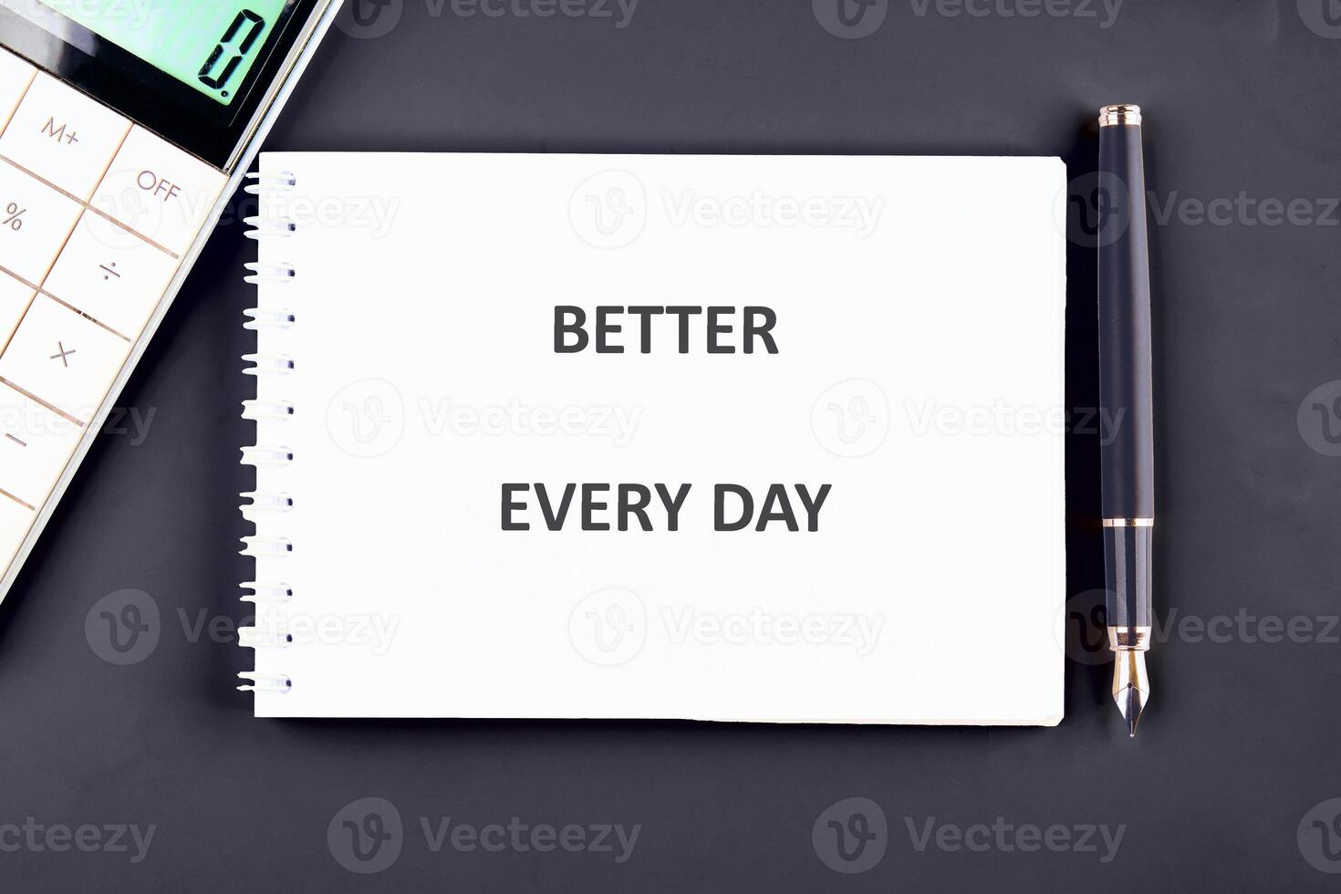 A notepad lays open, displaying the words Better Every Day. A calculator sits next to it, along with a sleek pen, creating a motivating workspace atmosphere perfect for productivity photo