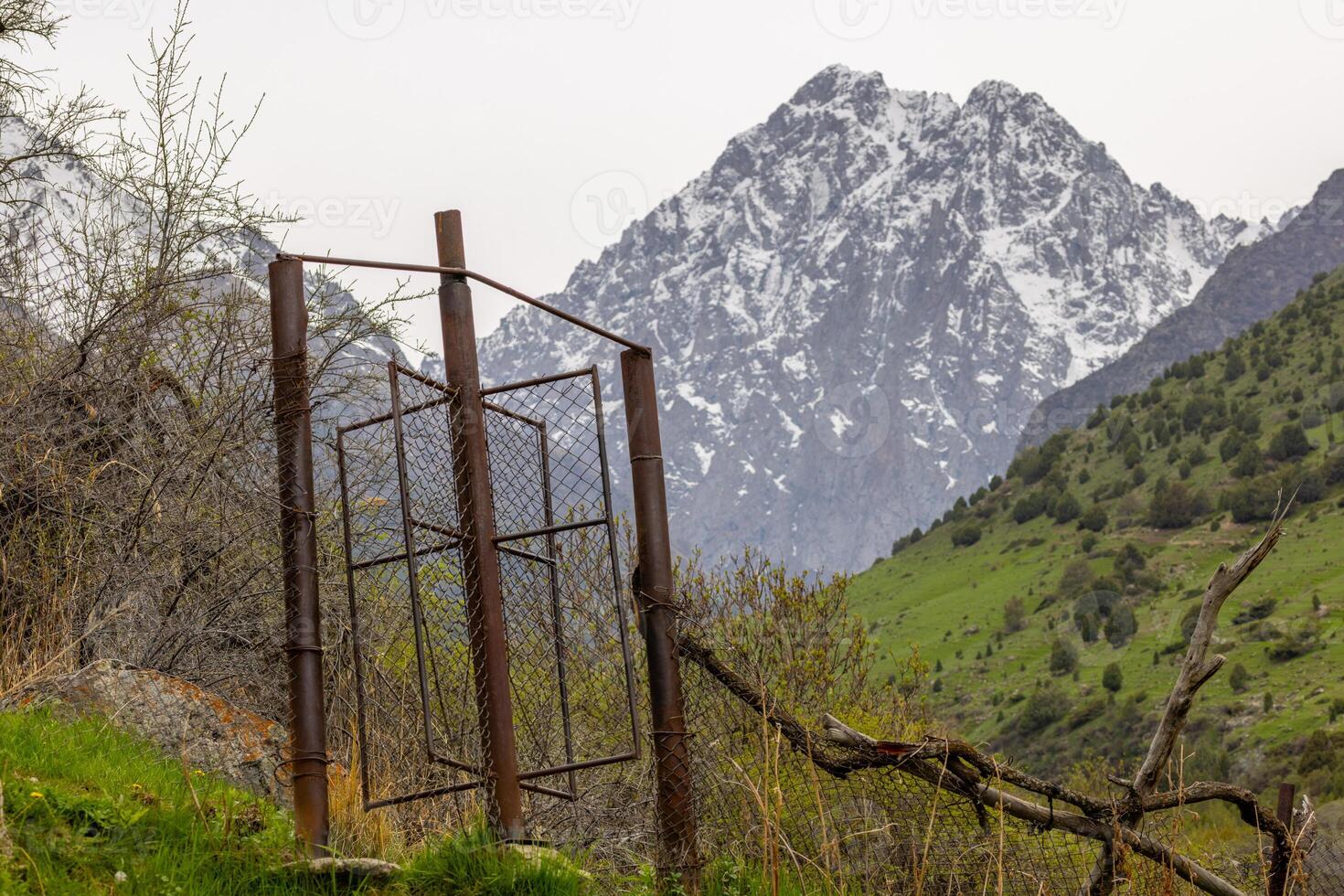 Rusty chain link fence with rotating gate in mountains of Kyrgyzstan. This gate is keeping cattle from passing, but leaving a way for people. photo