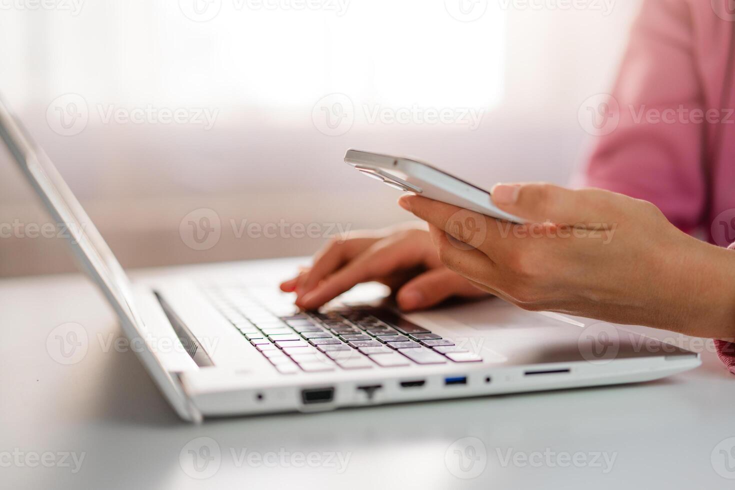 Hands type on a laptop keyboard while holding a smartphone, showcasing multitasking in a modern work environment. photo