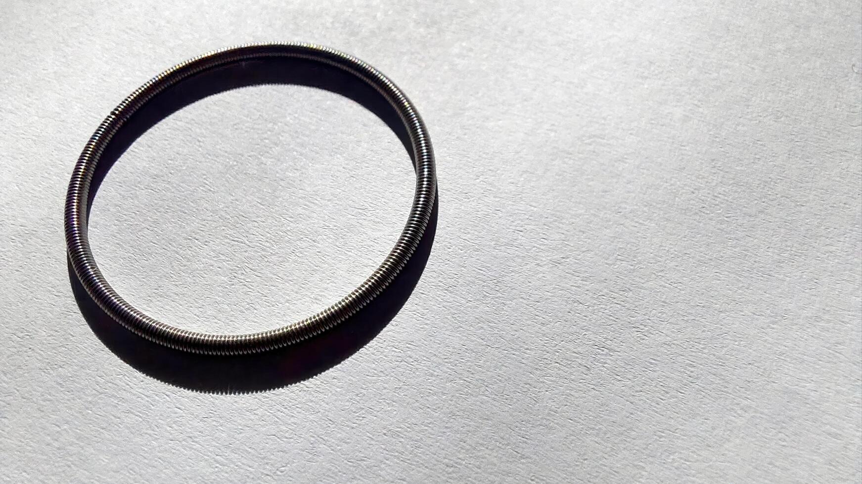 Round spring resting on smooth paper surface with gentle light casting shadow photo