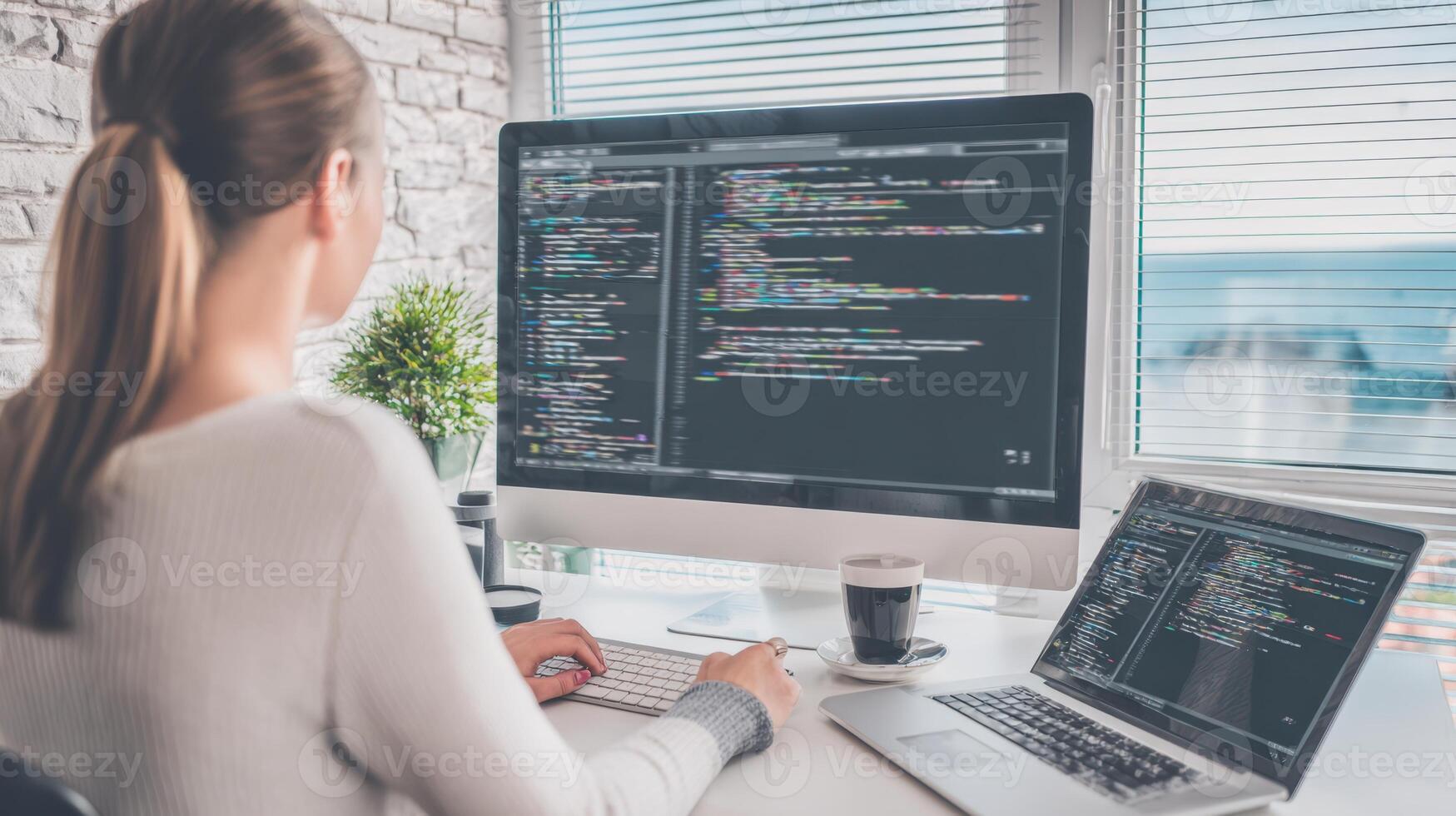 Female programmer working on coding with dual monitors and laptop in bright modern office photo