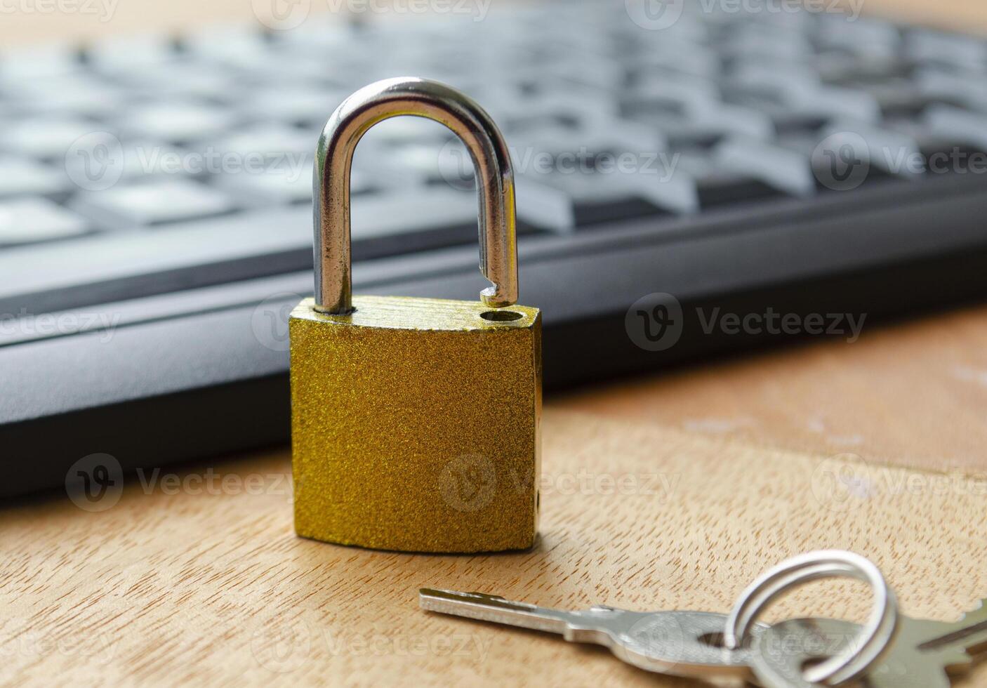 A golden padlock close up on a wooden desk beside a keyboard representing data privacy, internet safety and online access restriction. photo