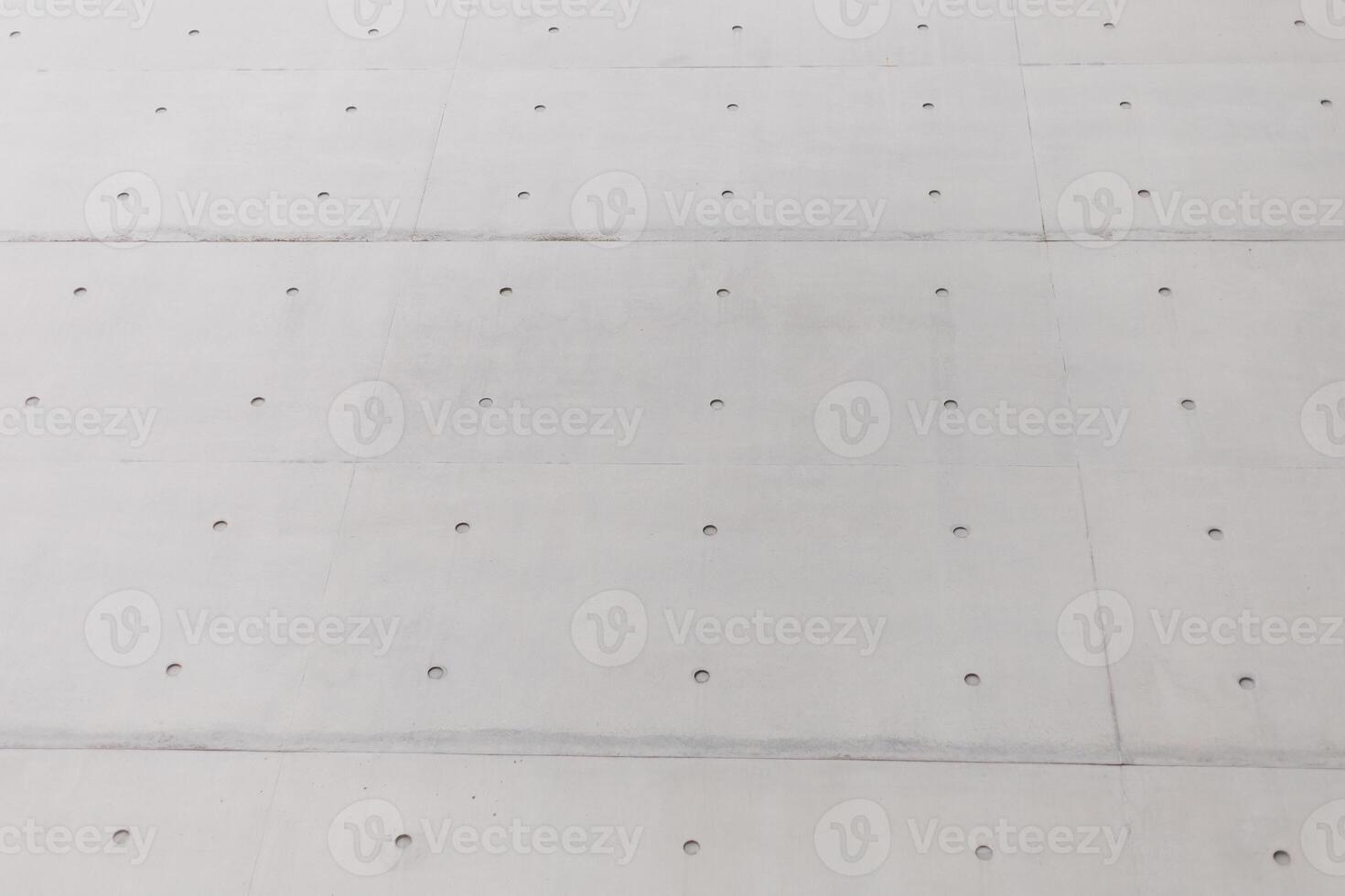 The view showcases a smooth concrete wall featuring an array of small, evenly spaced holes. The structure reflects contemporary design elements of an urban environment photo