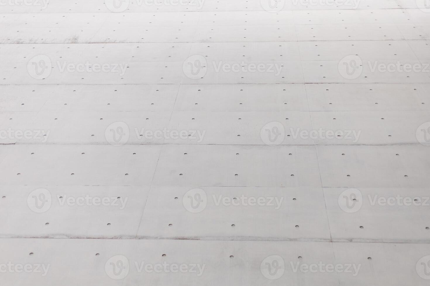 A close-up view of a concrete surface features evenly spaced holes. The setting suggests a construction area, illuminated by bright sunlight, highlighting the texture photo