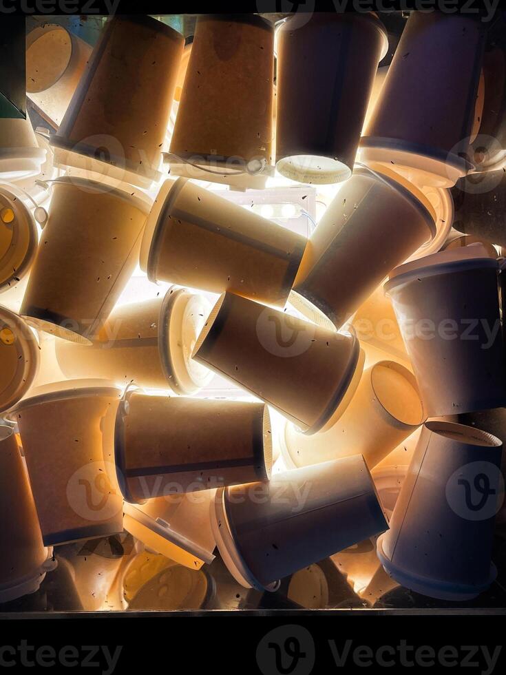 A collection of disposable coffee cups is stacked closely together and illuminated from behind, creating a dramatic lighting effect. The image highlights the texture and shape of. photo