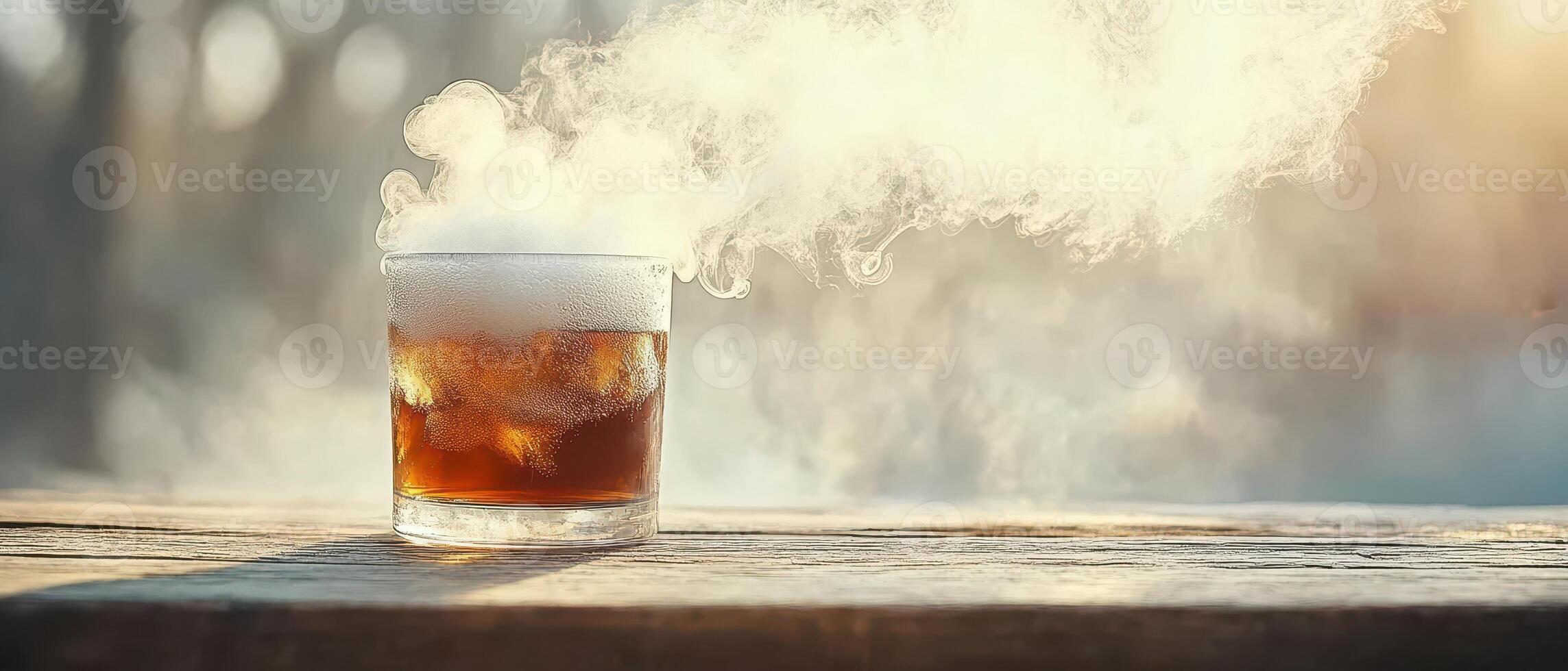 Cold beverage in glass. Refreshing liquid with ice on wooden surface. Steam rises creating a misty effect. Brown liquid on a sunny table. photo