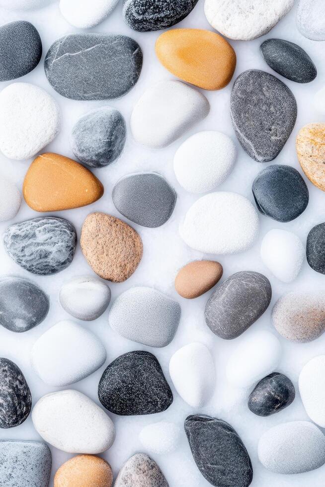 Smooth pebbles lie scattered on a soft white surface. Various rounded stones display natural colors and textures. Peaceful arrangement of earth toned elements. Close up view. photo