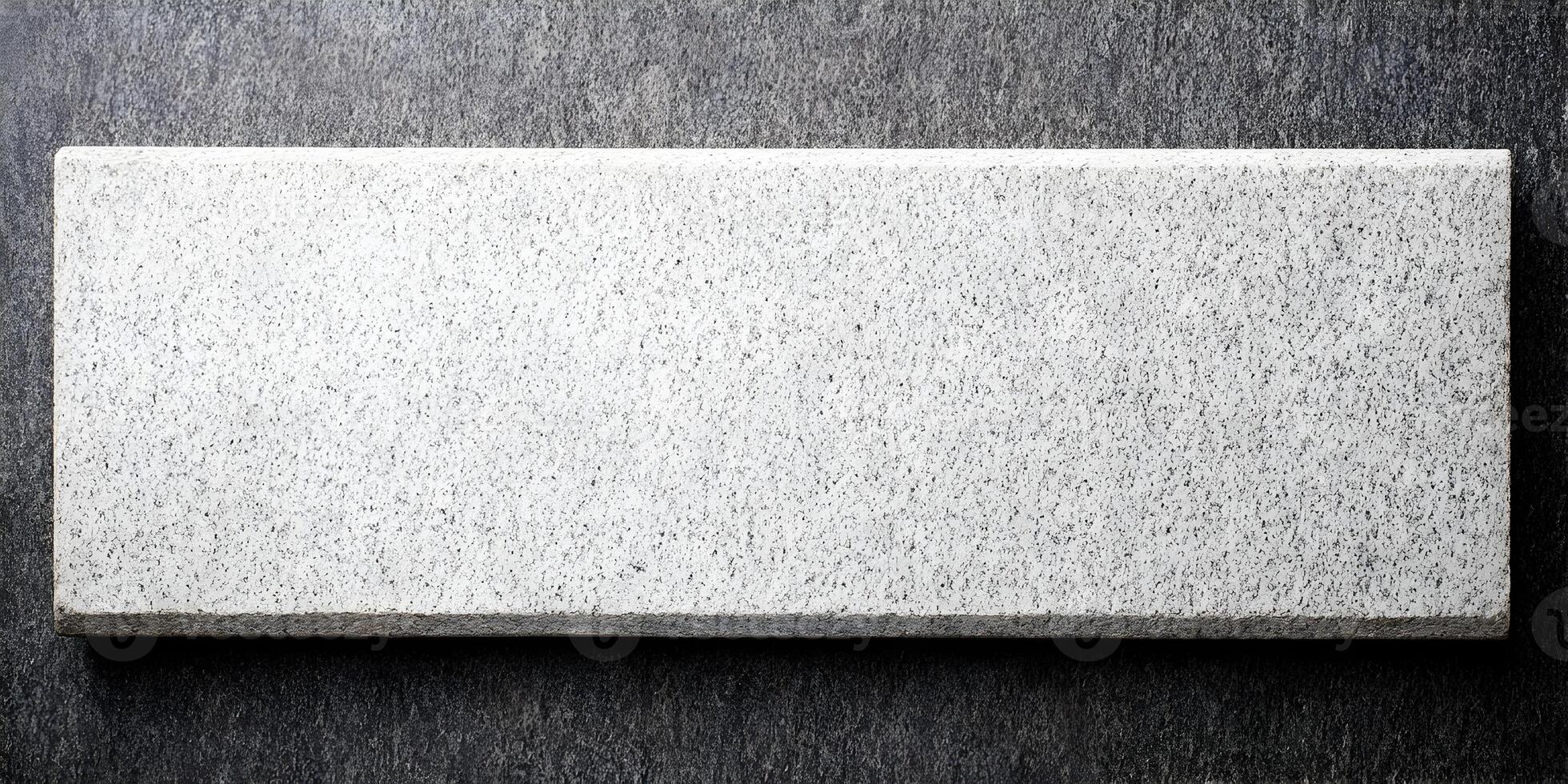 A rectangular light gray speckled granite block rests on a darker textured background photo