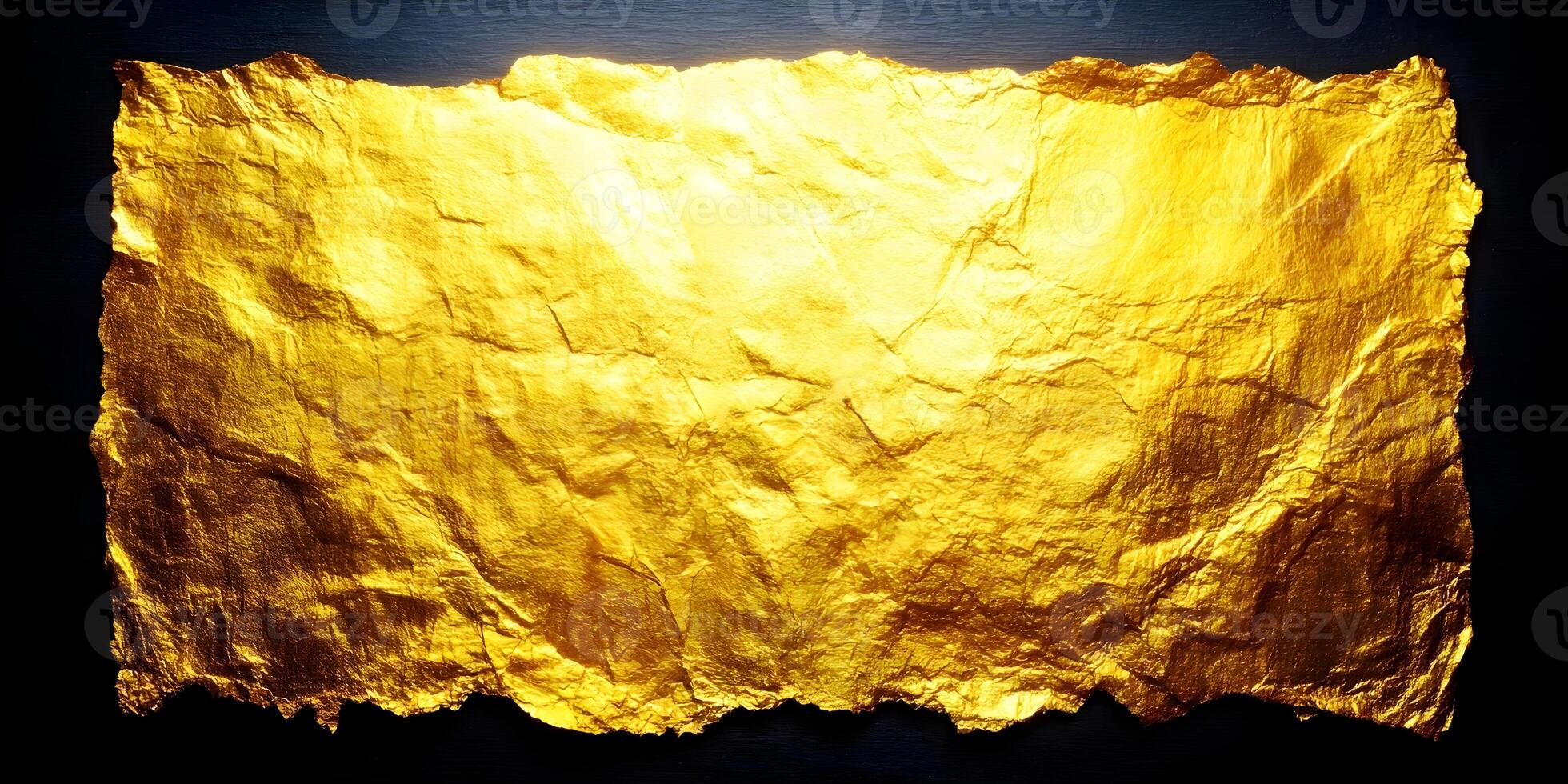 A sheet of shimmering crumpled gold foil with rough edges is illuminated against a dark background creating a luxurious texture photo