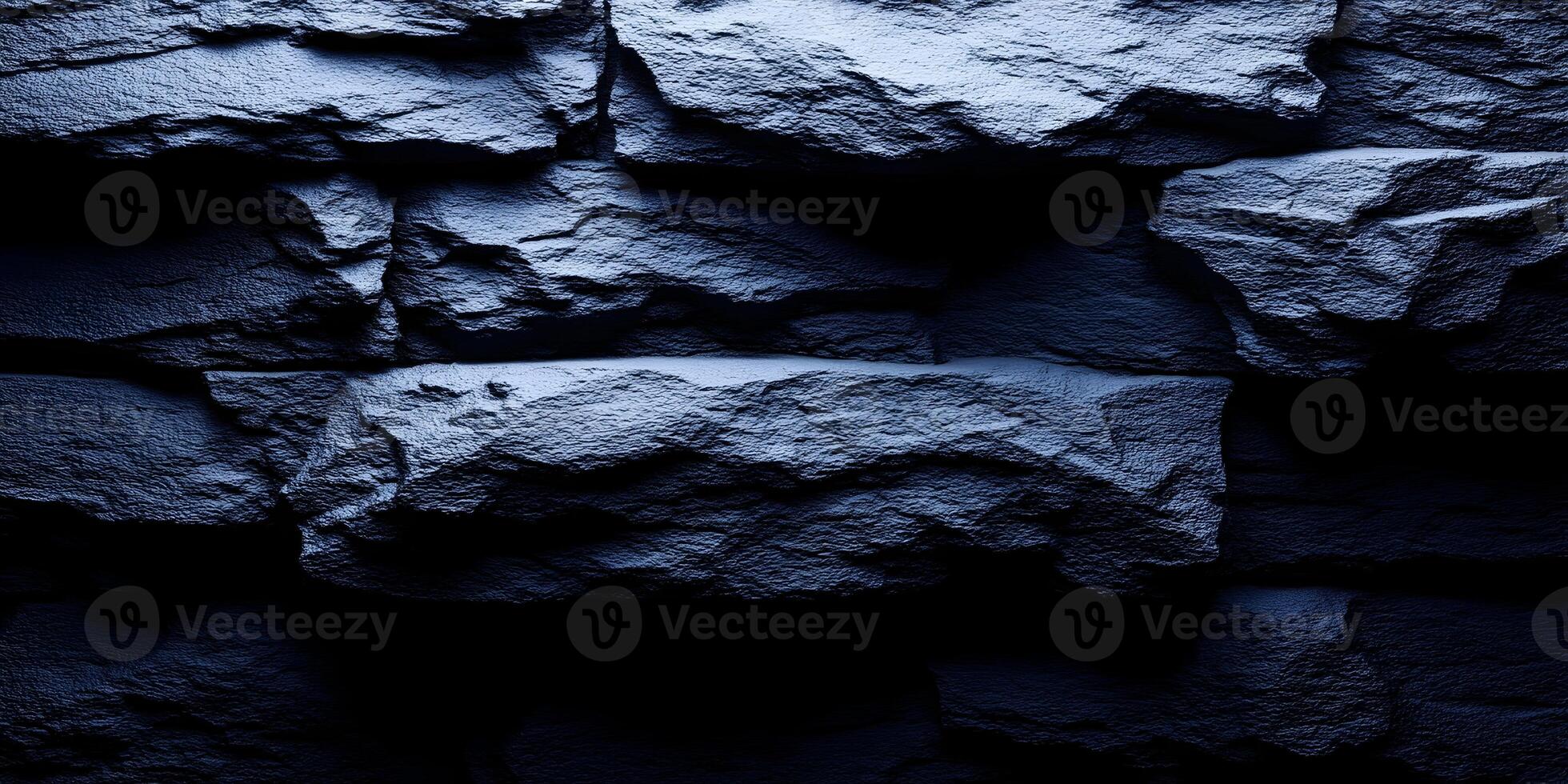 A dark blue rough stone wall texture features jagged rocks with dramatic light and shadow creating a moody abstract background photo