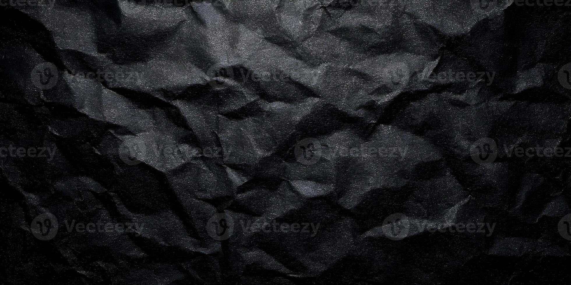 A dark abstract background features a heavily crumpled sheet of black paper creating a rough textured surface photo