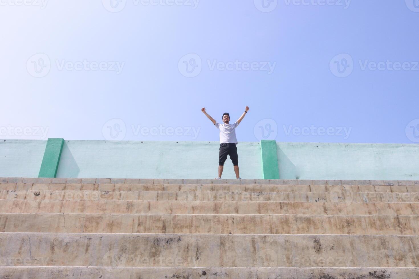 A man is standing on a set of stairs raise hands, looking up at the sky. He is smiling and he is happy photo