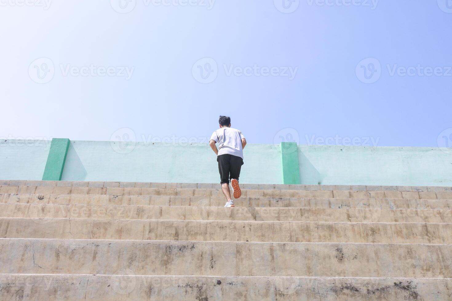A man is running up a set of stairs. Concept of determination and perseverance as the man pushes himself to reach the top of the steps. The man's, focused expression. photo