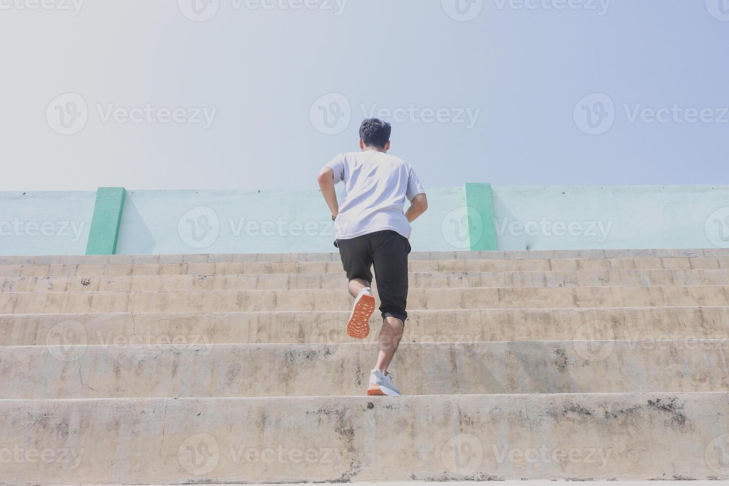 A man is running up a set of stairs. Concept of determination and perseverance as the man pushes himself to reach the top of the steps. The man's focused, expression. photo
