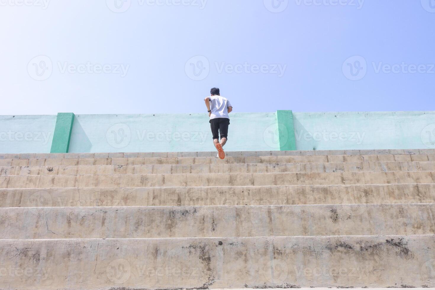A man is running up a set of stairs. Concept of determination and perseverance as the man pushes himself to reach the top of the steps. The man's focused expression, photo