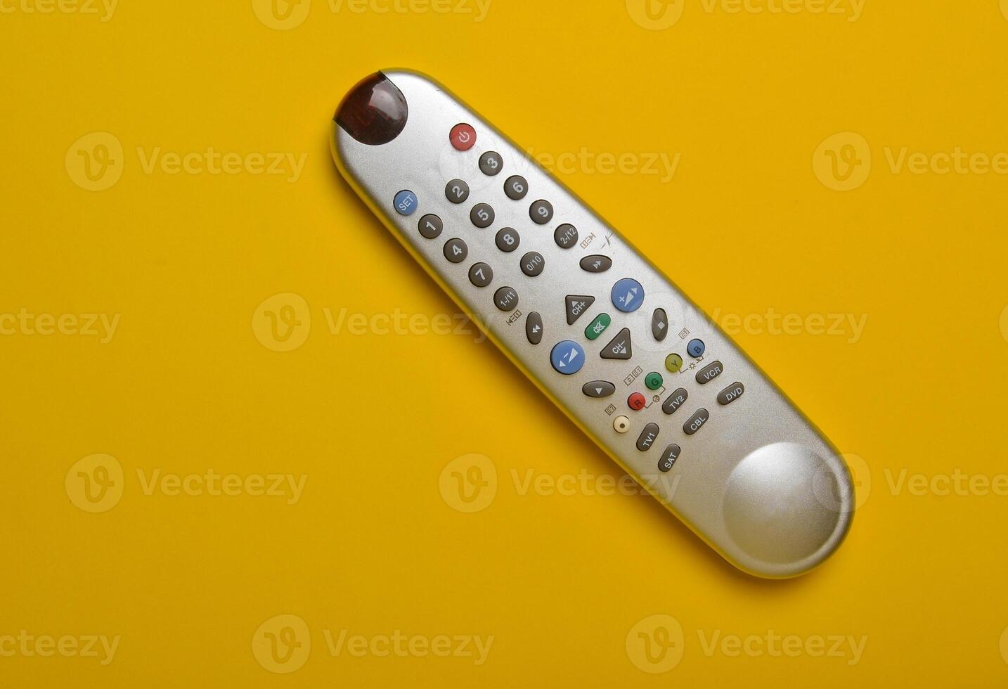 Multi-function push-button TV remote control on a yellow paper background. Top view. photo