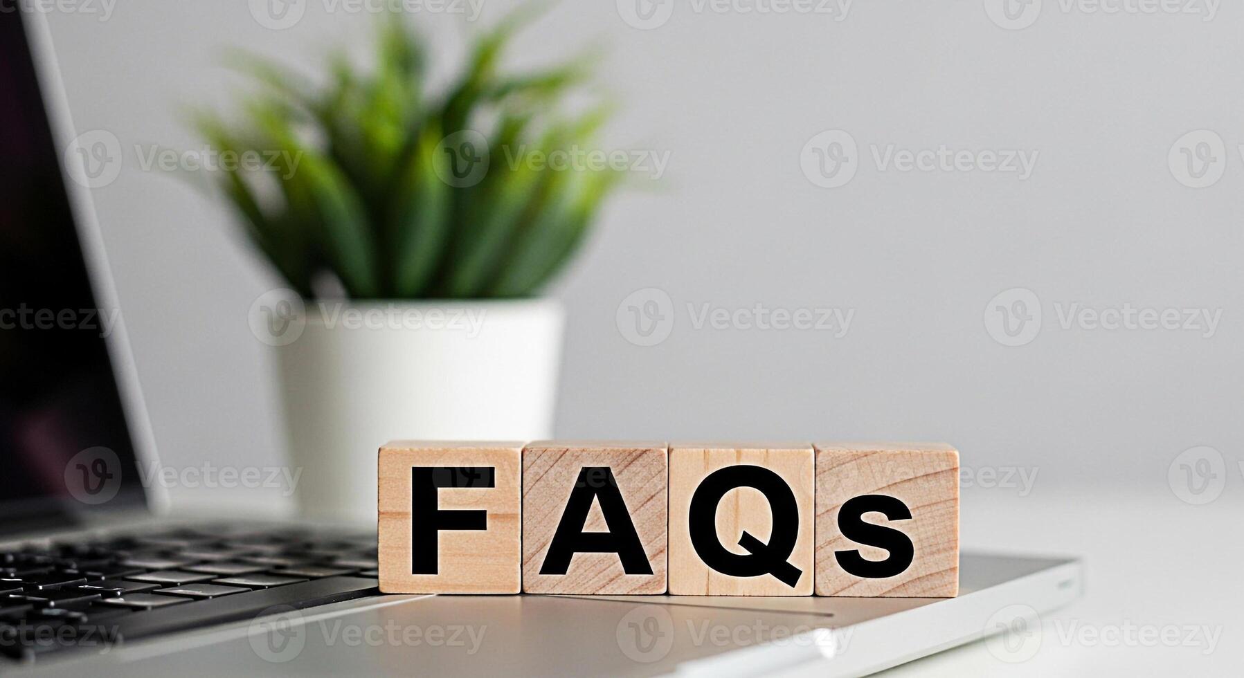 Wooden blocks displaying FAQs on a laptop keyboard in a bright office setting symbolizing readily available information and customer support for online queries and common questions photo