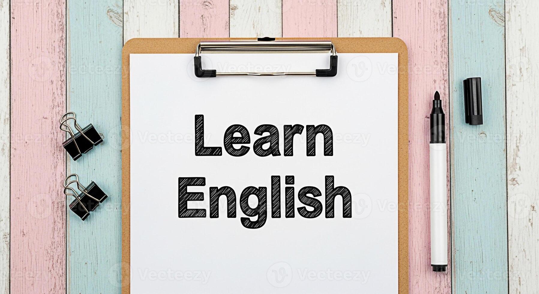 Clipboard displaying Learn English on a colorful wooden desk with a marker and binder clips creating a learning environment and promoting the concept of language acquisition and educational resources photo
