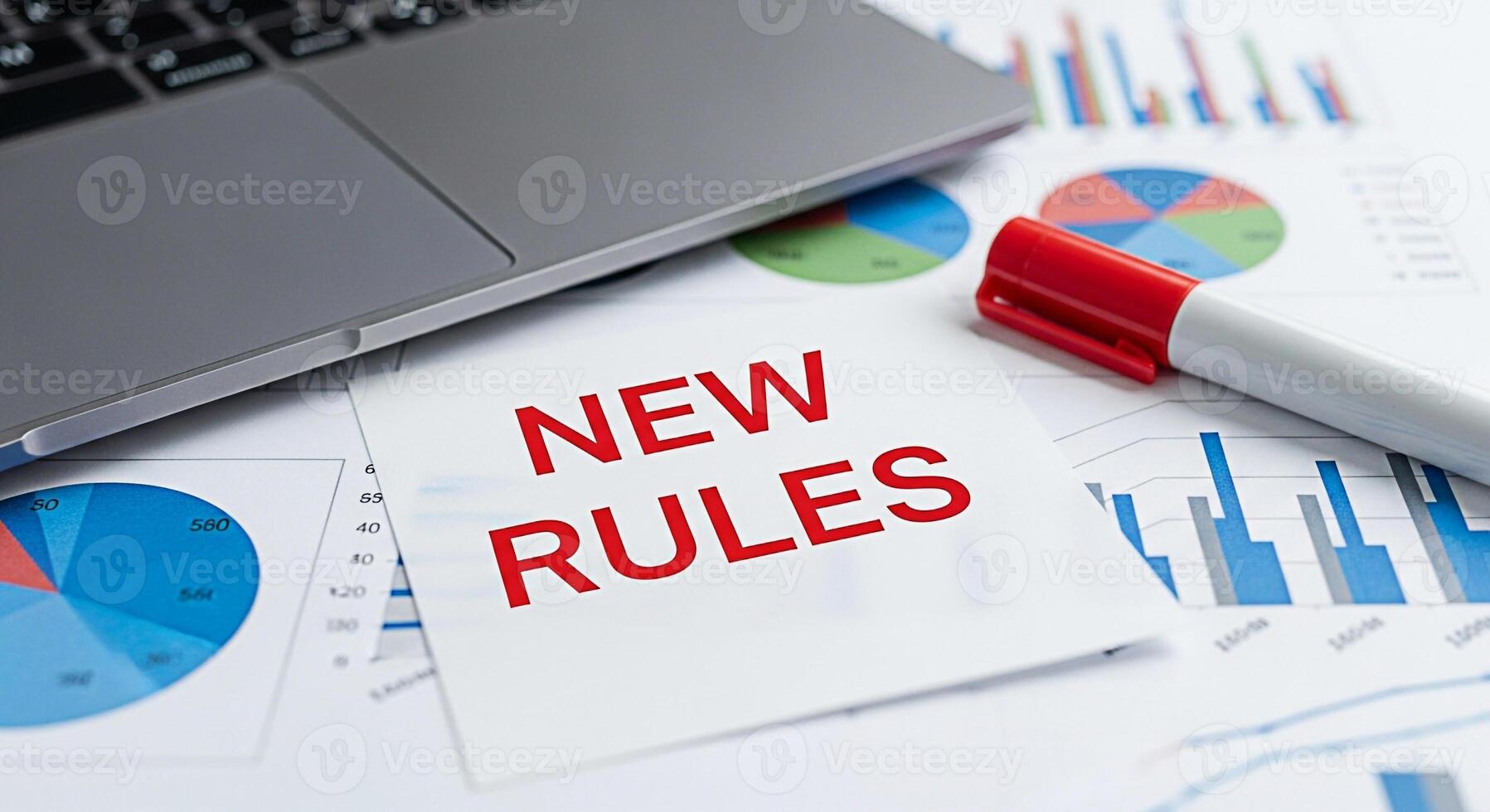 Laptop rests on financial reports with a note displaying New Rules and a red marker symbolizing change and adaptation in a datadriven business environment fostering a sense of strategic planning and i photo