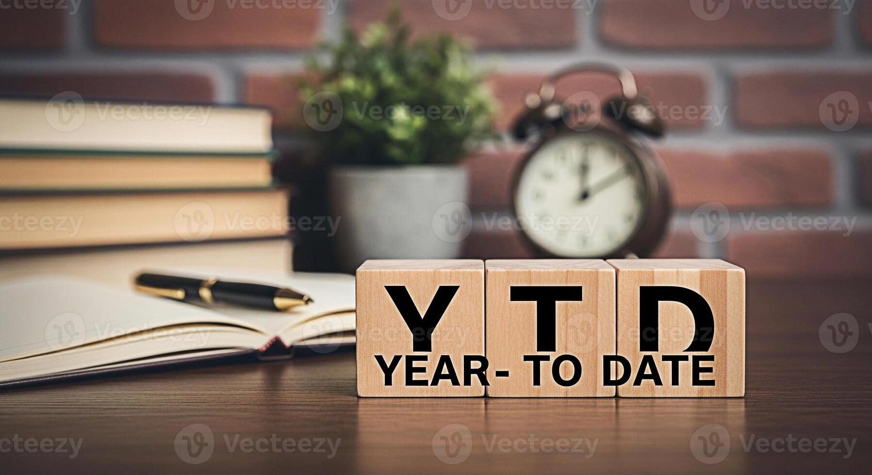 Wooden blocks displaying YTD YearToDate on a desk with books a pen a plant and an alarm clock in a cozy office setting representing financial performance and business progress photo