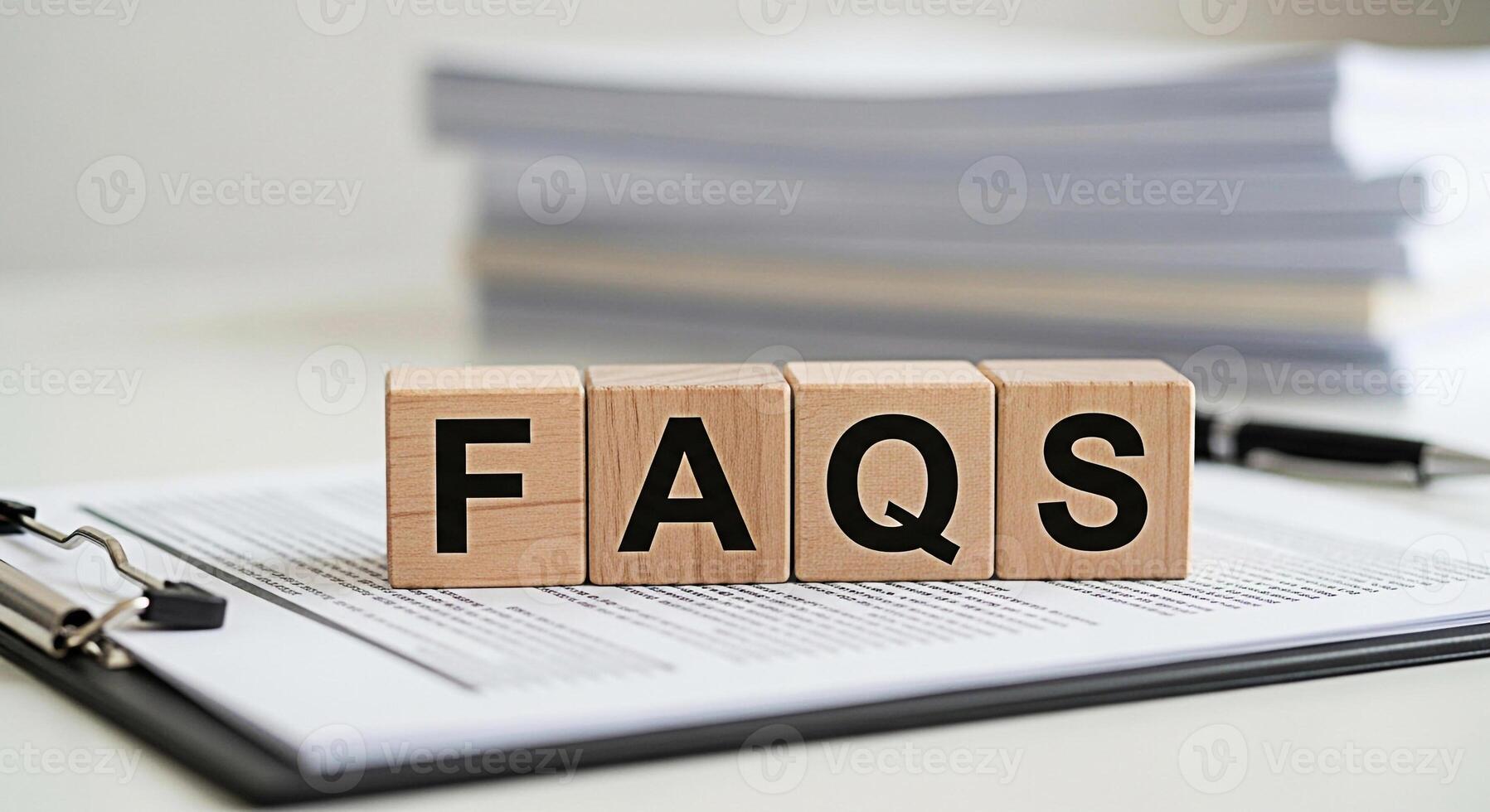 Wooden blocks spelling FAQs resting on a clipboard with a document in a bright office setting representing frequently asked questions and providing helpful information for customers and clients photo