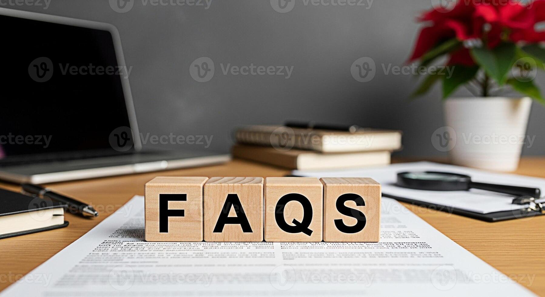 Wooden blocks spelling FAQs on a desk with laptop books and poinsettia representing frequently asked questions and information resources in a professional and helpful office environment photo