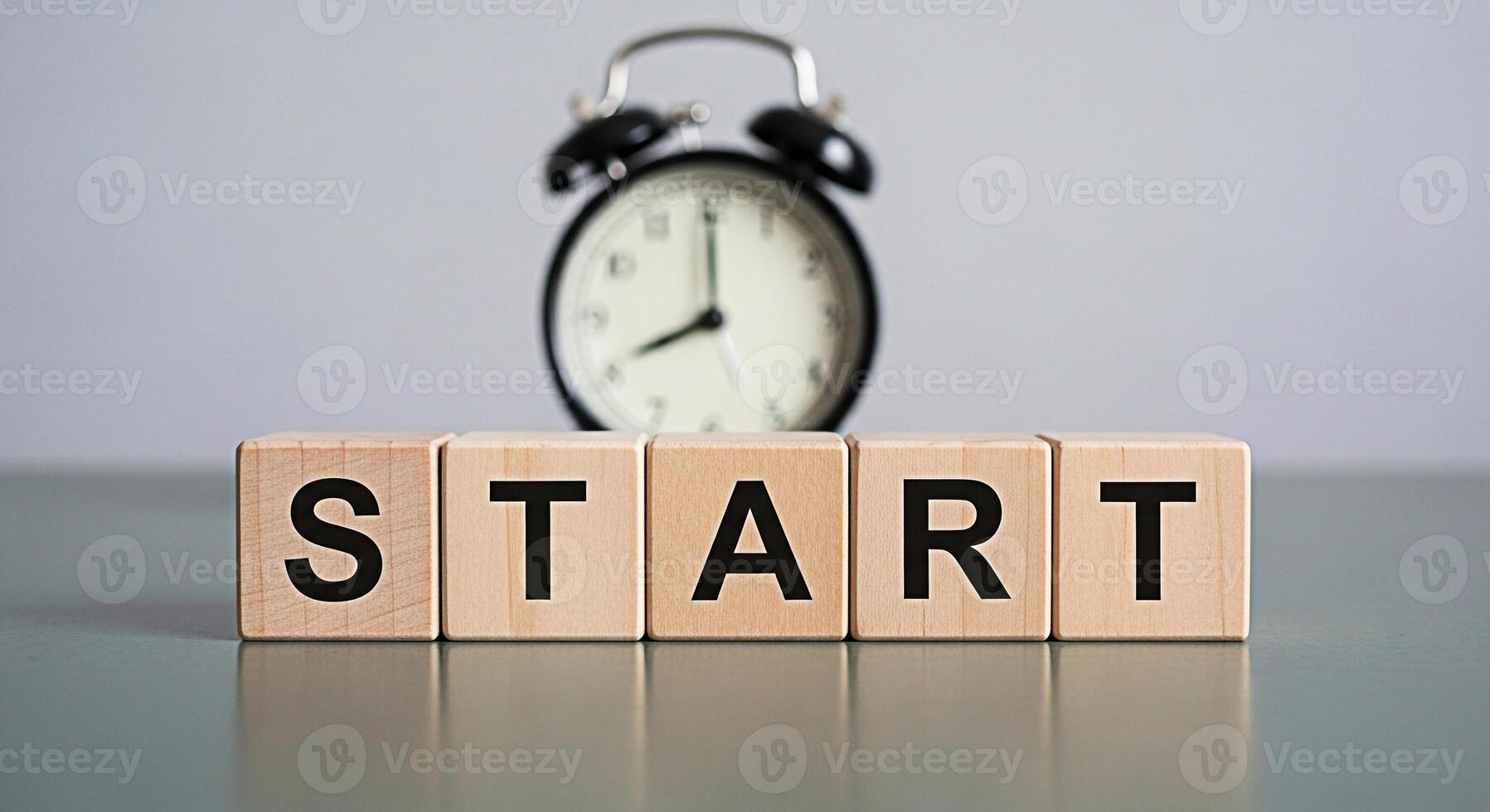 Wooden blocks spelling START with a blurred alarm clock in the background on a gray surface symbolizing a fresh beginning and the importance of time management for achieving goals photo