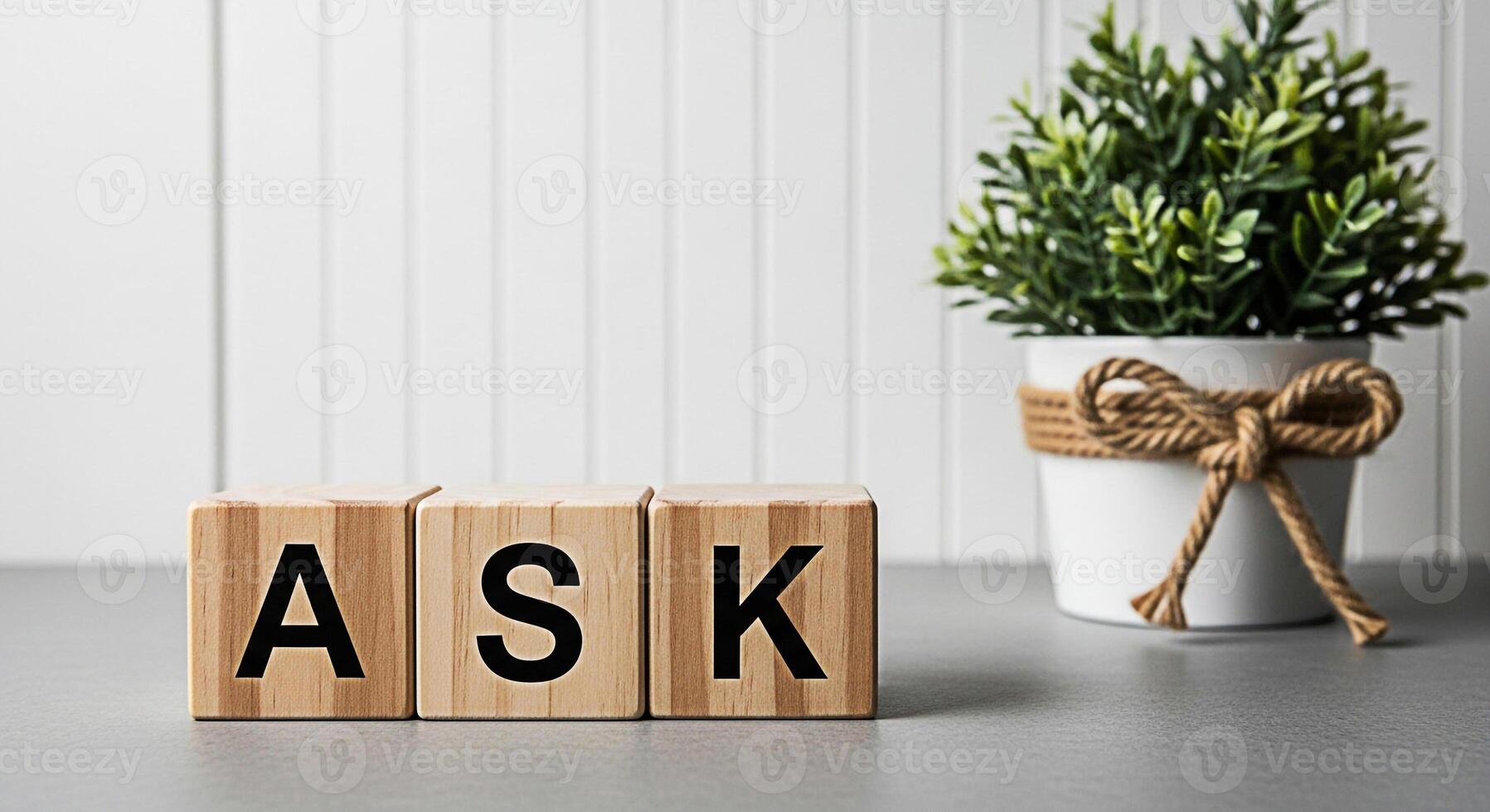 Wooden blocks spelling ASK on a gray surface in a bright minimalist room representing questions curiosity and the pursuit of knowledge with a decorative potted plant adding a touch of nature photo