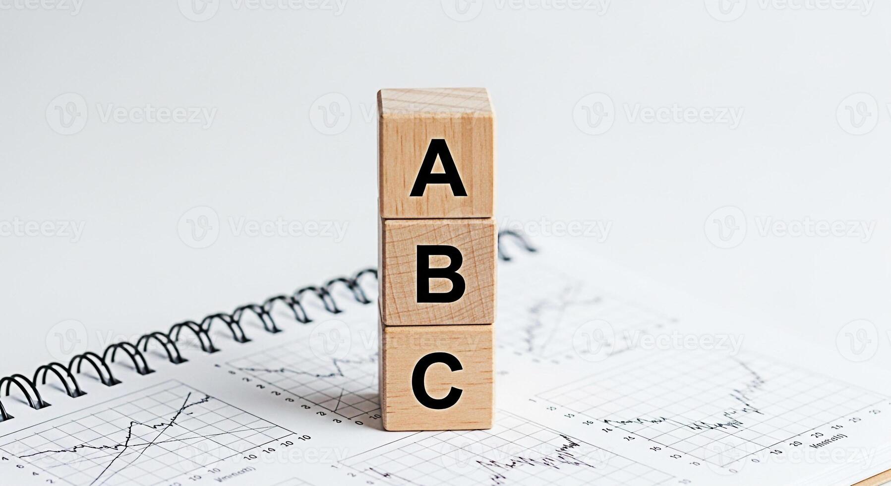 Wooden ABC blocks stacked on a spiral notebook with financial charts representing basic concepts in business analytics and education in a clean minimalist and bright studio setting photo