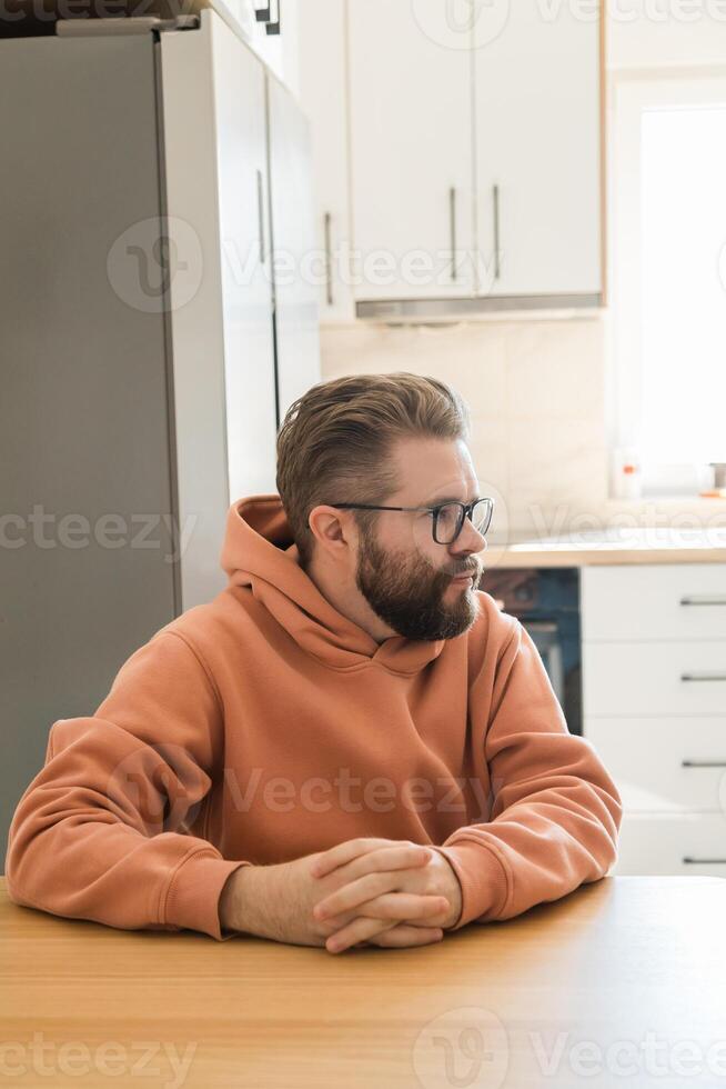 Man looking sideways while sitting at kitchen table. Visual metaphor of listening, awareness, concentration, interpersonal communication and reflective thinking in daily context. photo
