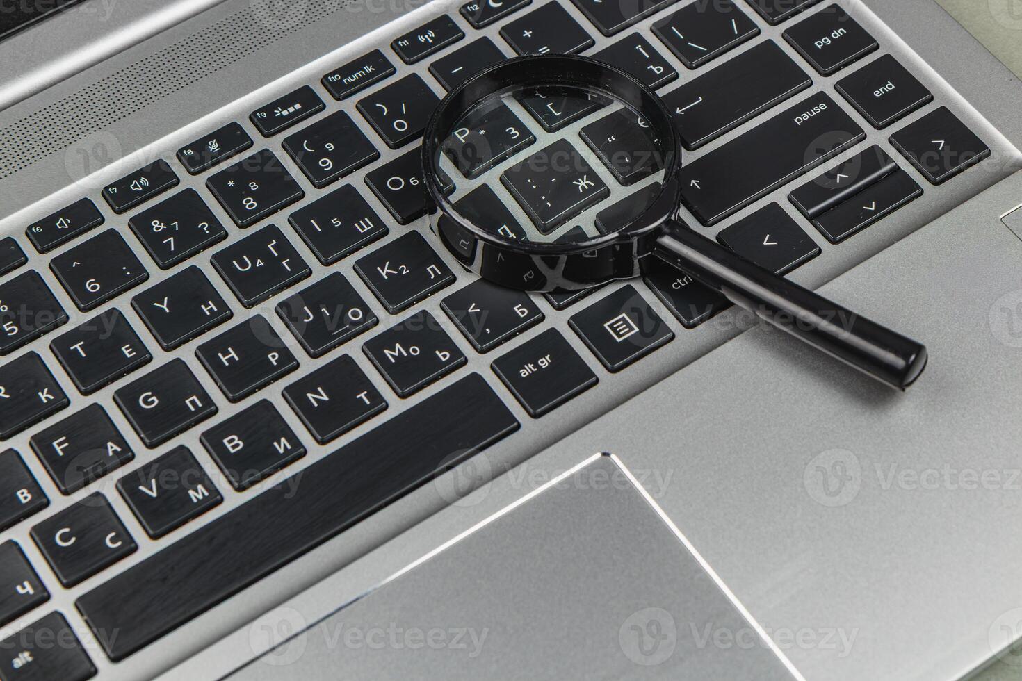 Magnifying glass on a laptop keyboard showing different characters and keys photo