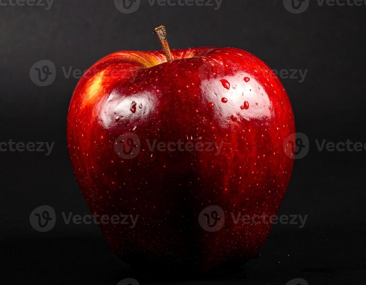 Close up studio shot of single dark red apple with water droplets centered on black background showing rich color and smooth texture photo
